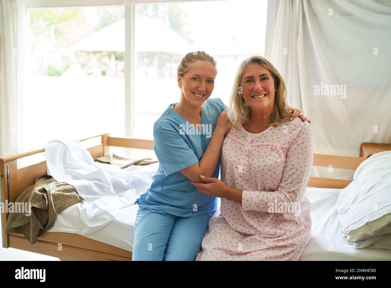 Porträt einer lächelnden Pflegekraft, die eine bettsitzende ältere Frau im Rehabilitationszentrum umarmt Stockfoto