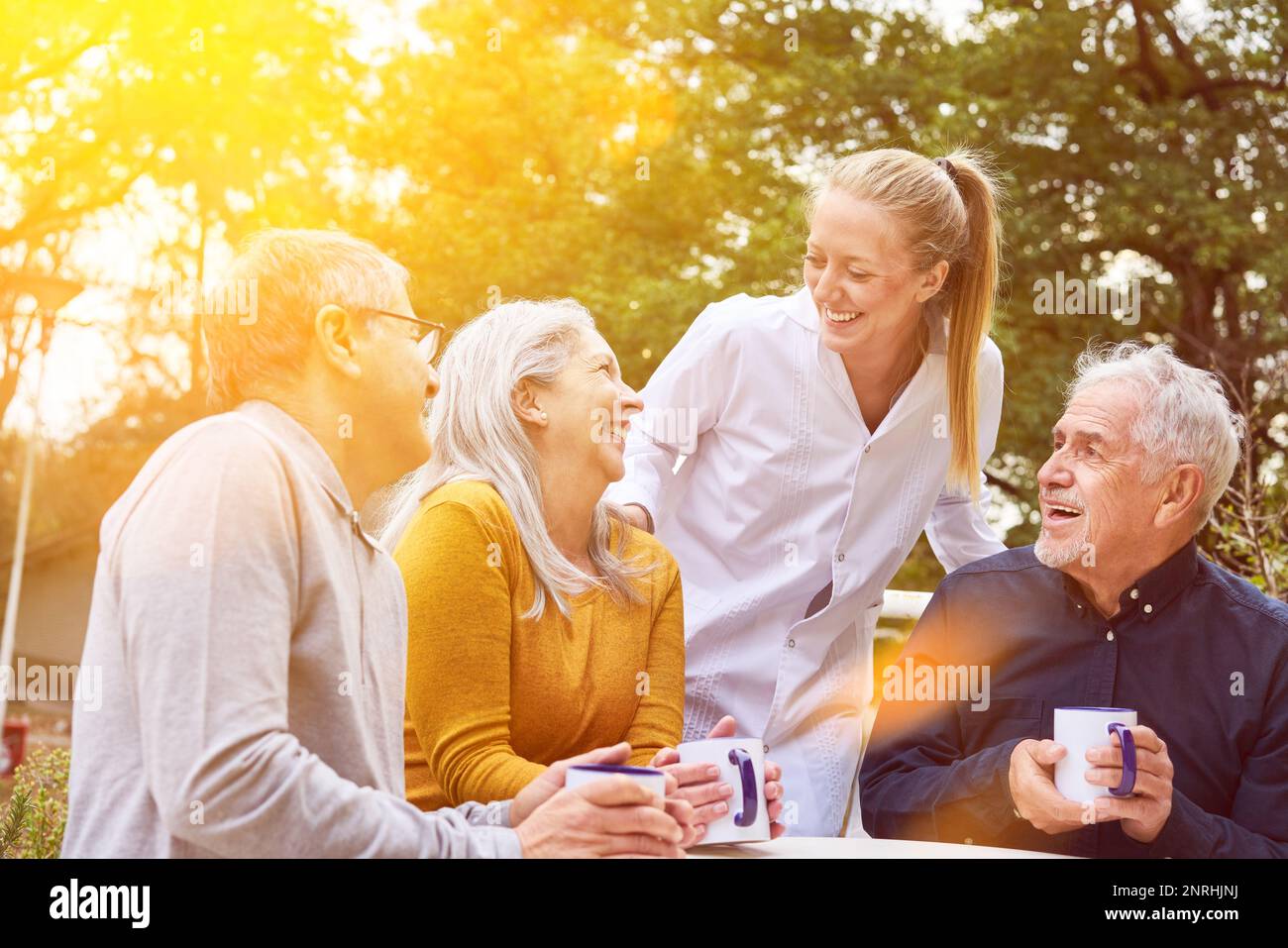 Glückliche Seniorengruppe, die im Garten des Pflegeheims mit einer Krankenschwester lacht Stockfoto