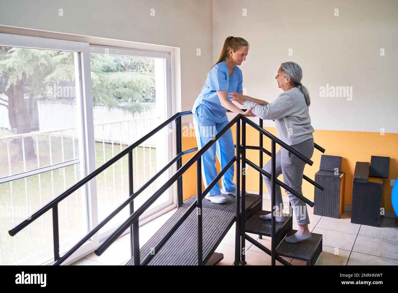 Lächelnde junge Therapeutin, die ältere Frau in der Bewegungstherapie im Rehabilitationszentrum unterstützt Stockfoto
