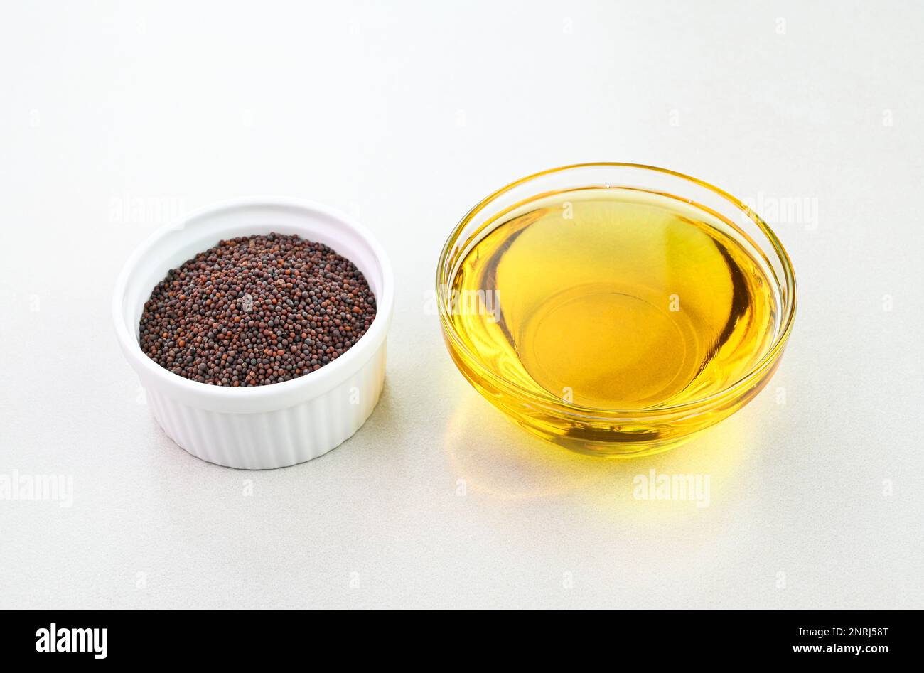 Senfsamenöl in einem Glasbecher mit Senfkörnern in einer Schüssel Stockfoto