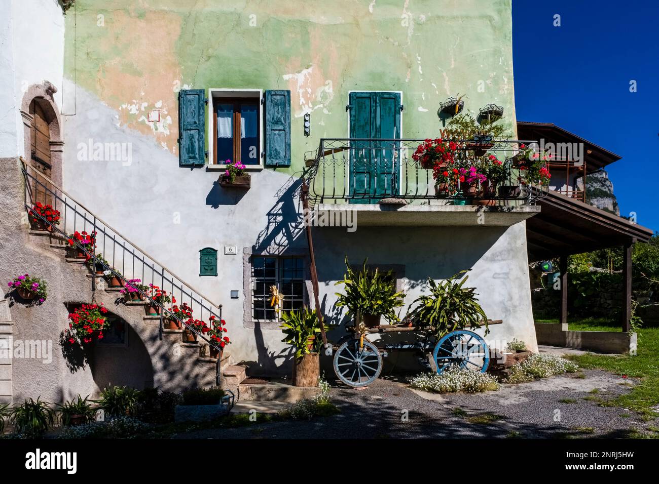 Fassade eines traditionellen Bauernhauses mit Treppe, Balkon und Blumen in einem kleinen Dorf. Stockfoto