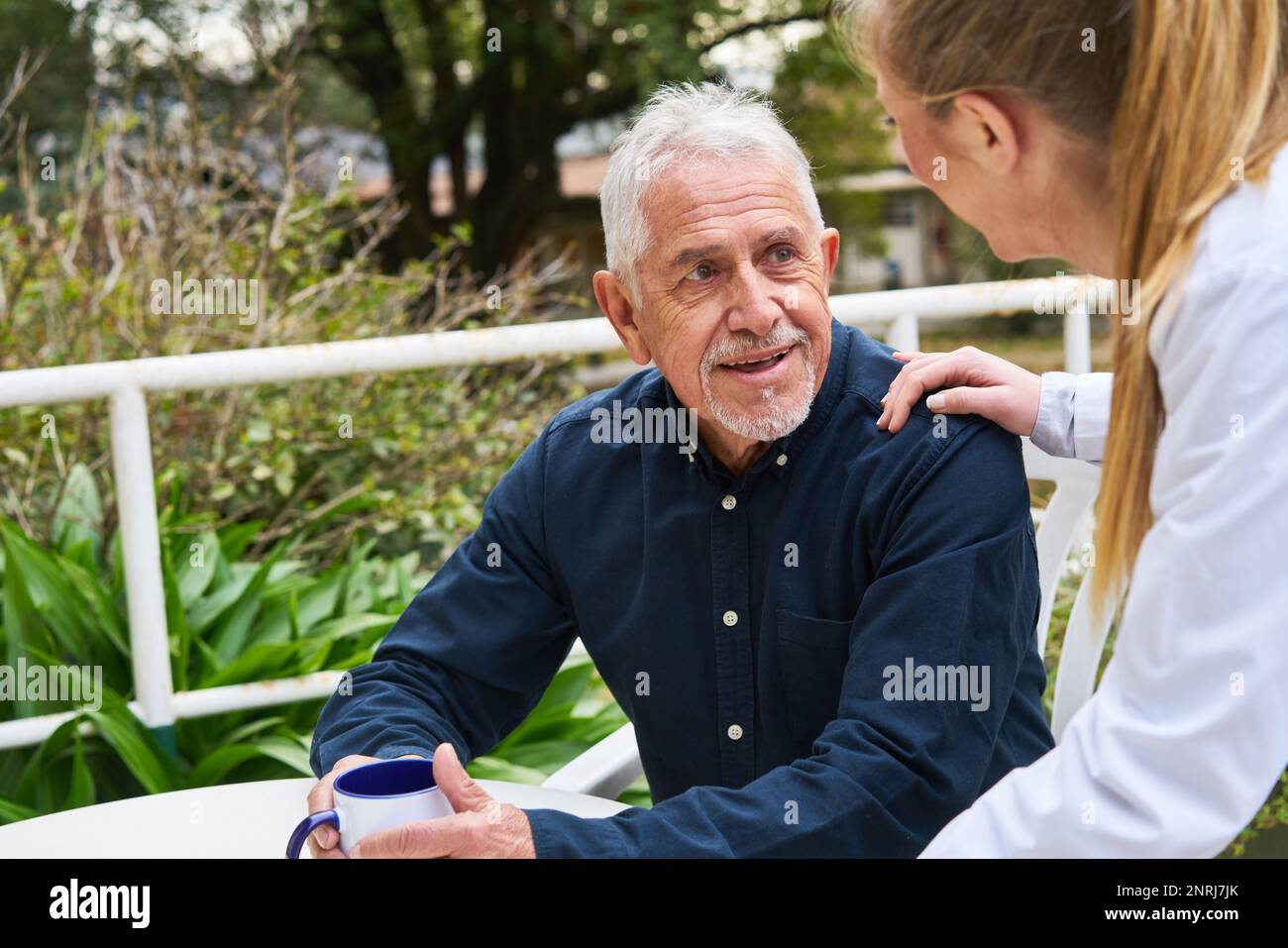 Lächelnde Arztin im Garten des Pflegeheims sitzender älterer Mann Stockfoto