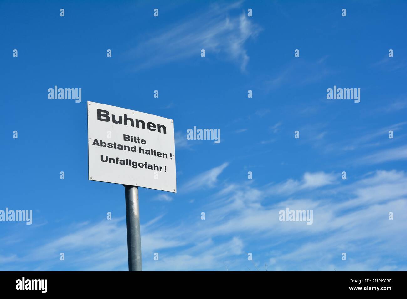 Hinweisschild in deutscher Schrift 'Buhnen - Bitte halten Sie Abstand - Unfallgefahr' mit blauem Himmel Stockfoto