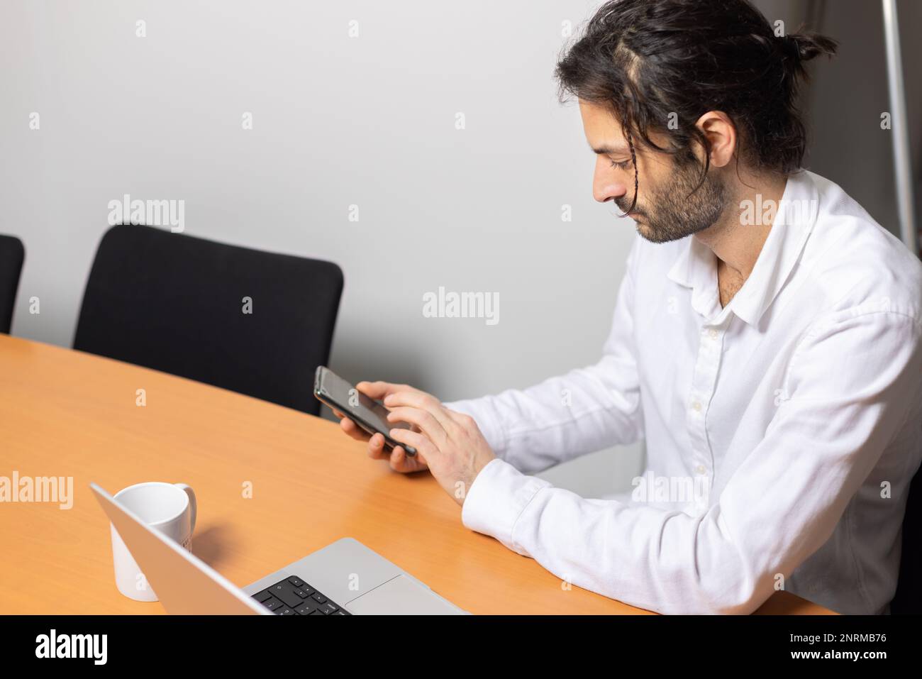 Porträt eines Mannes, der an seinem Laptop arbeitet und mit seinem Telefon kommuniziert. Er sitzt in einem schönen Büro Stockfoto