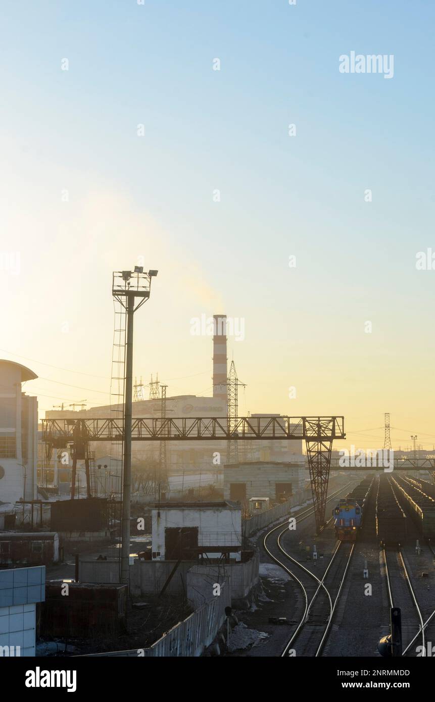 Fabrikgebäude und Rohrleitungen eines Kohlekraftwerks am Stadtrand in der Nähe der Bahngleise bei Sonnenuntergang in Russland. Stockfoto