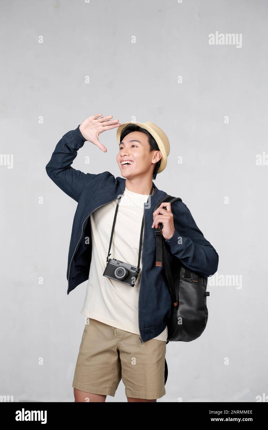 Ein hübscher junger Mann mit Rucksack, der in die Ferne blickt. Seine Hand bedeckt die Augen vor der Sonne Stockfoto