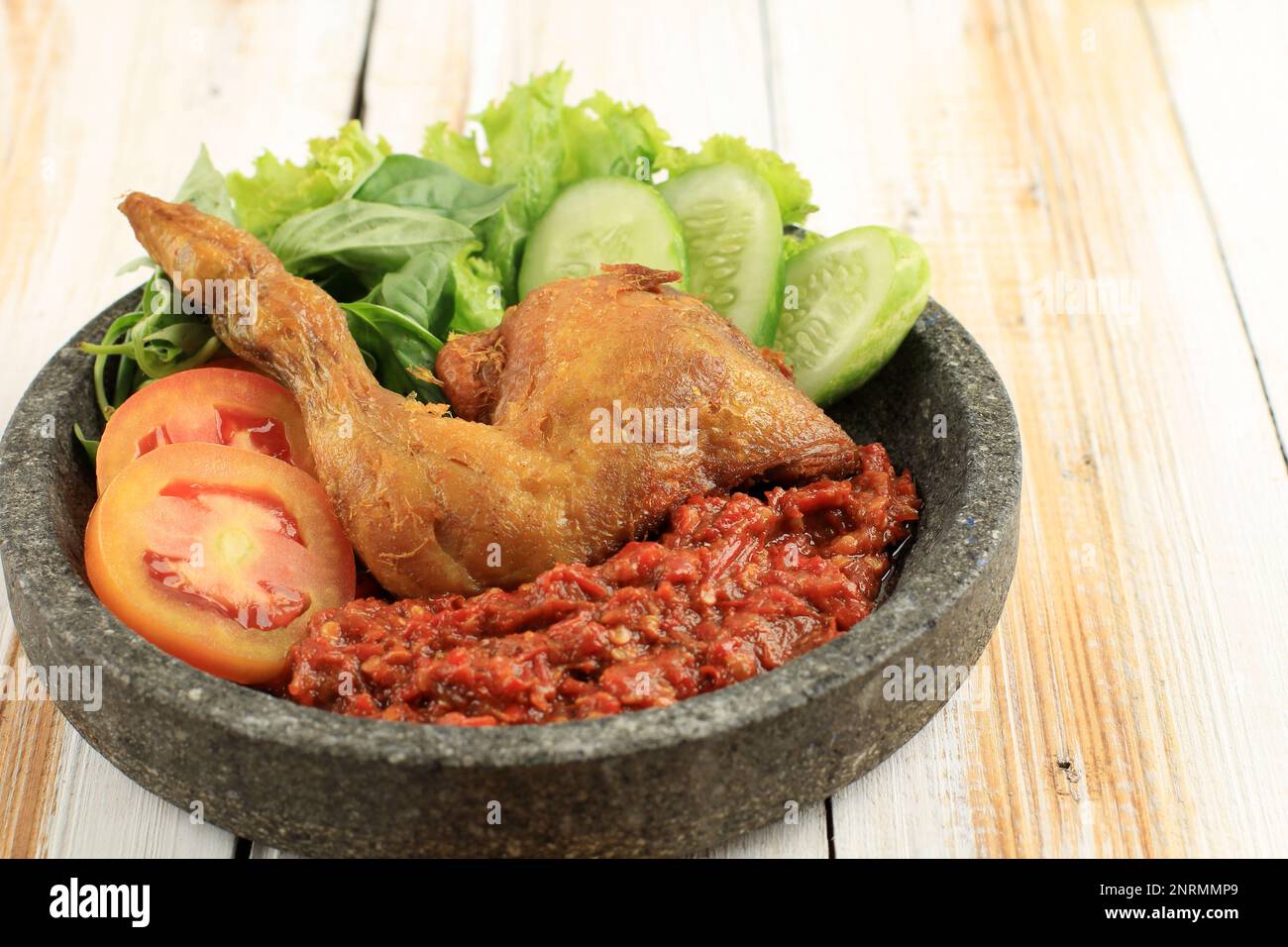 Ayam Penyet oder Penyetan Ayam, gebratenes Hühnchen serviert mit scharfem Sambal auf einem Holztisch Stockfoto