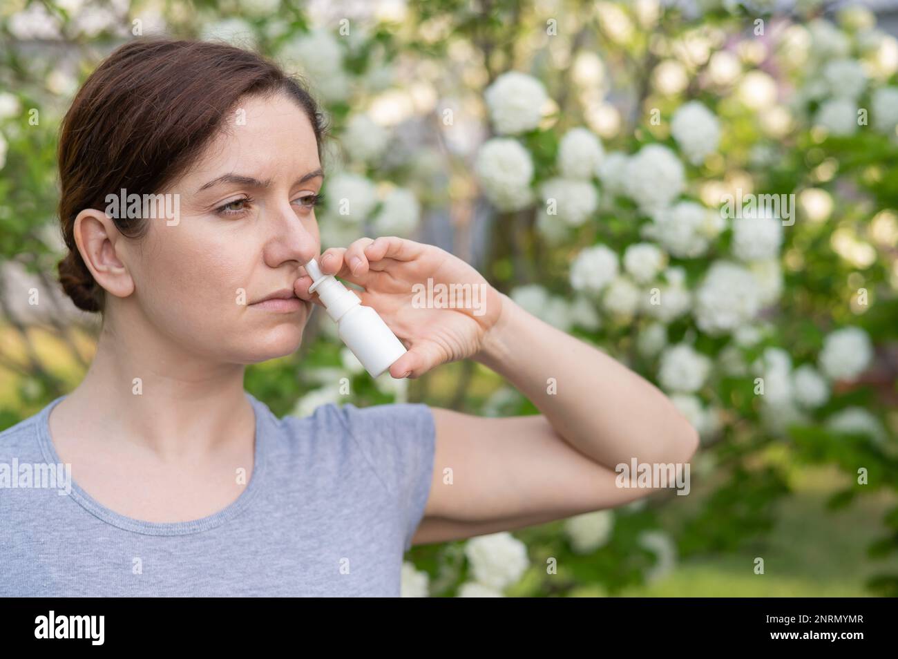 Kaukasische Frau verwendet ein Nasenspray, während sie im Park spazieren geht. Stockfoto