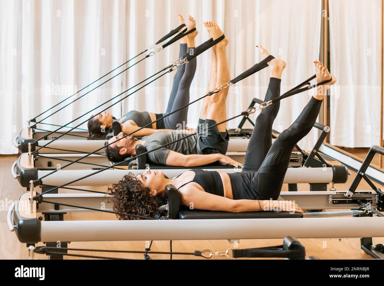 Der ganze Körper konzentrierter Menschen in der Aktivkleidung, die während des Trainings im Fitnessstudio Übungen auf Pilates-Geräten machen Stockfoto
