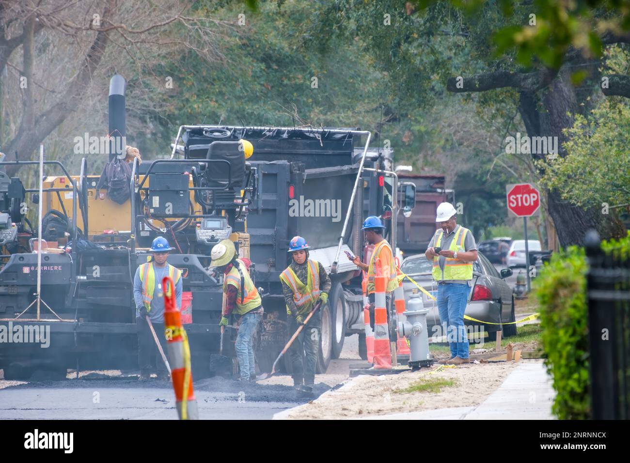 NEW ORLEANS, LA, USA - 20. FEBRUAR 2023: Arbeiter verteilen heißen, rauchenden Asphalt auf der Straßenoberfläche hinter schweren Maschinen während Straßenreparaturprojekten Stockfoto