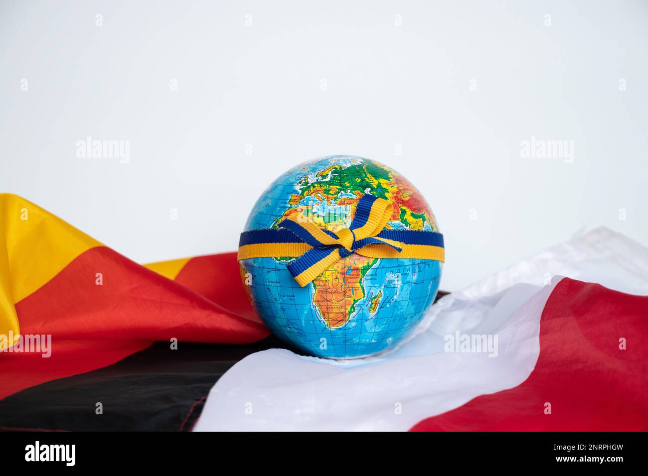 Der mit einem Band verbundene Globus mit der Flagge der Ukraine liegt auf den Flaggen Deutschlands und Polens auf weißem Hintergrund Stockfoto