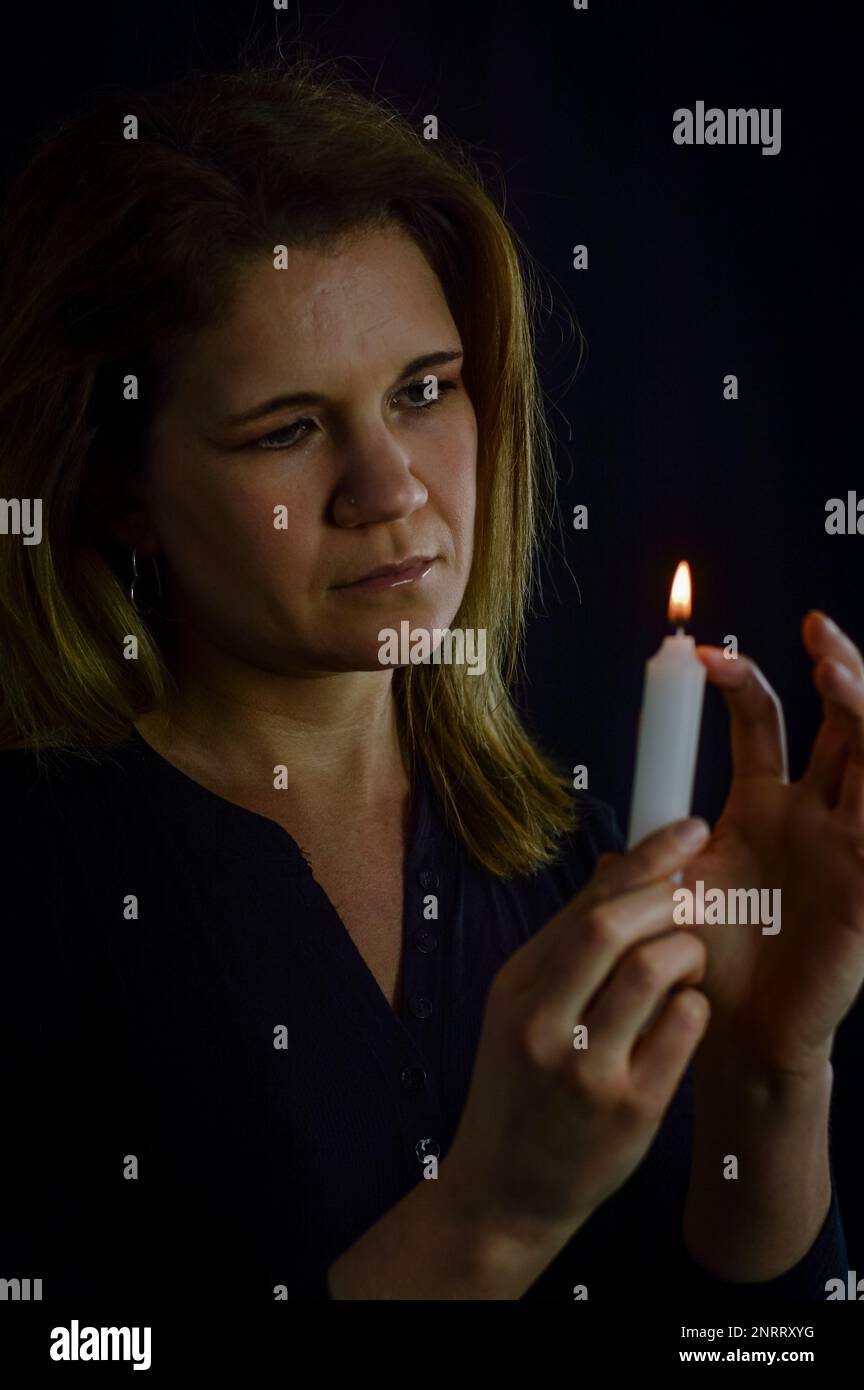 Porträt einer Frau, die mit einer Kerzenflamme und tropfendem Wachs spielt Stockfoto