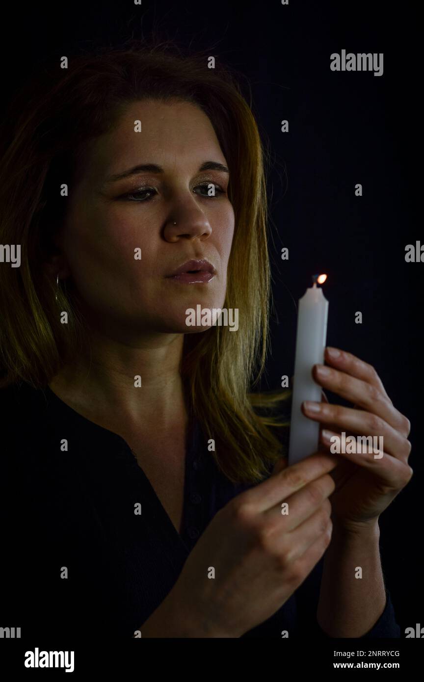 Porträt einer schönen blonden Frau, die die Flamme einer Kerze in ihrer Hand ausbläst Stockfoto