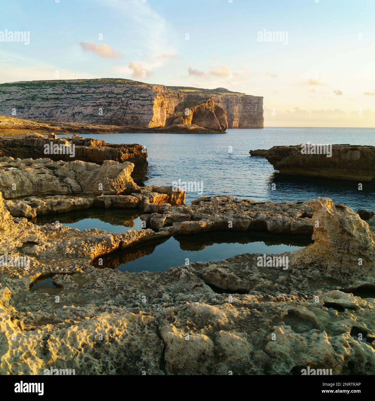 Dwejra, Insel Gozo, Malta. Atemberaubender Sonnenaufgang in der Nähe der Azure Window Ruinen. Warmes gelbes Sonnenlicht auf den Felsen und dem Meer, blau mit Wolken. Beruhige mich Stockfoto