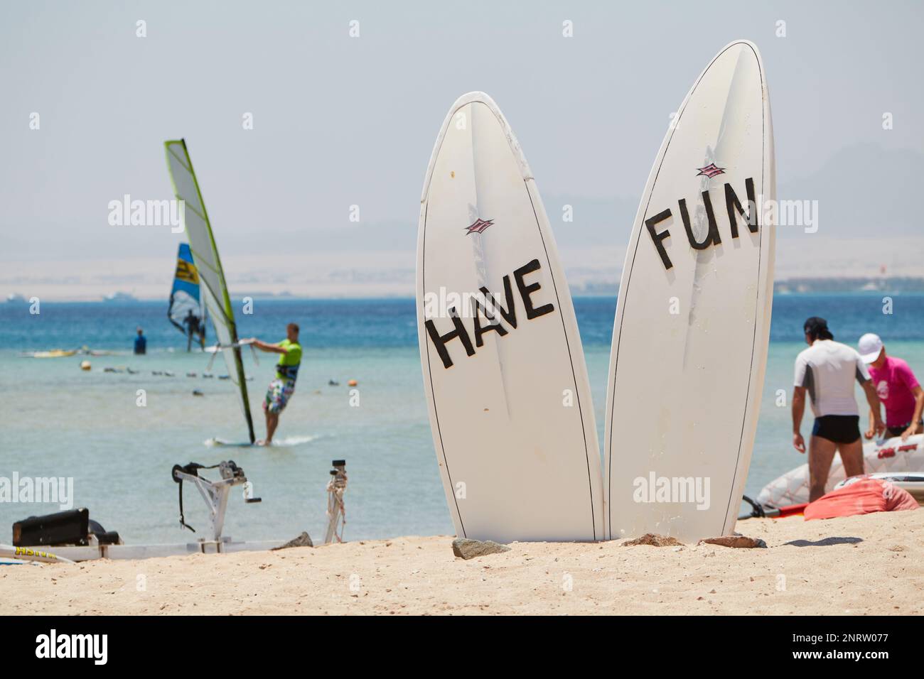 Zwei Surfbretter, auf denen „HAVE FUN“ geschrieben ist, an einem Strand in Soma Bay, Ägypten. Menschen im Hintergrund. Stockfoto