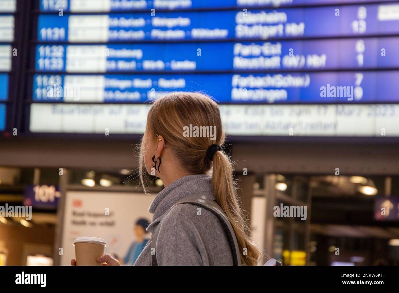 Junge Frau, die auf die Anzeigetafel eines Bahnhofs schaut (Modell freigegeben) Stockfoto