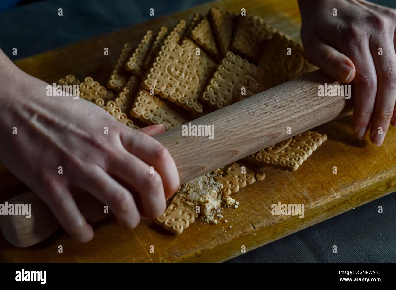 Hände, die Kekse mit einer Walznadel zerbrechen, um die knusprige Basis eines Käsekuchen zuzubereiten Stockfoto