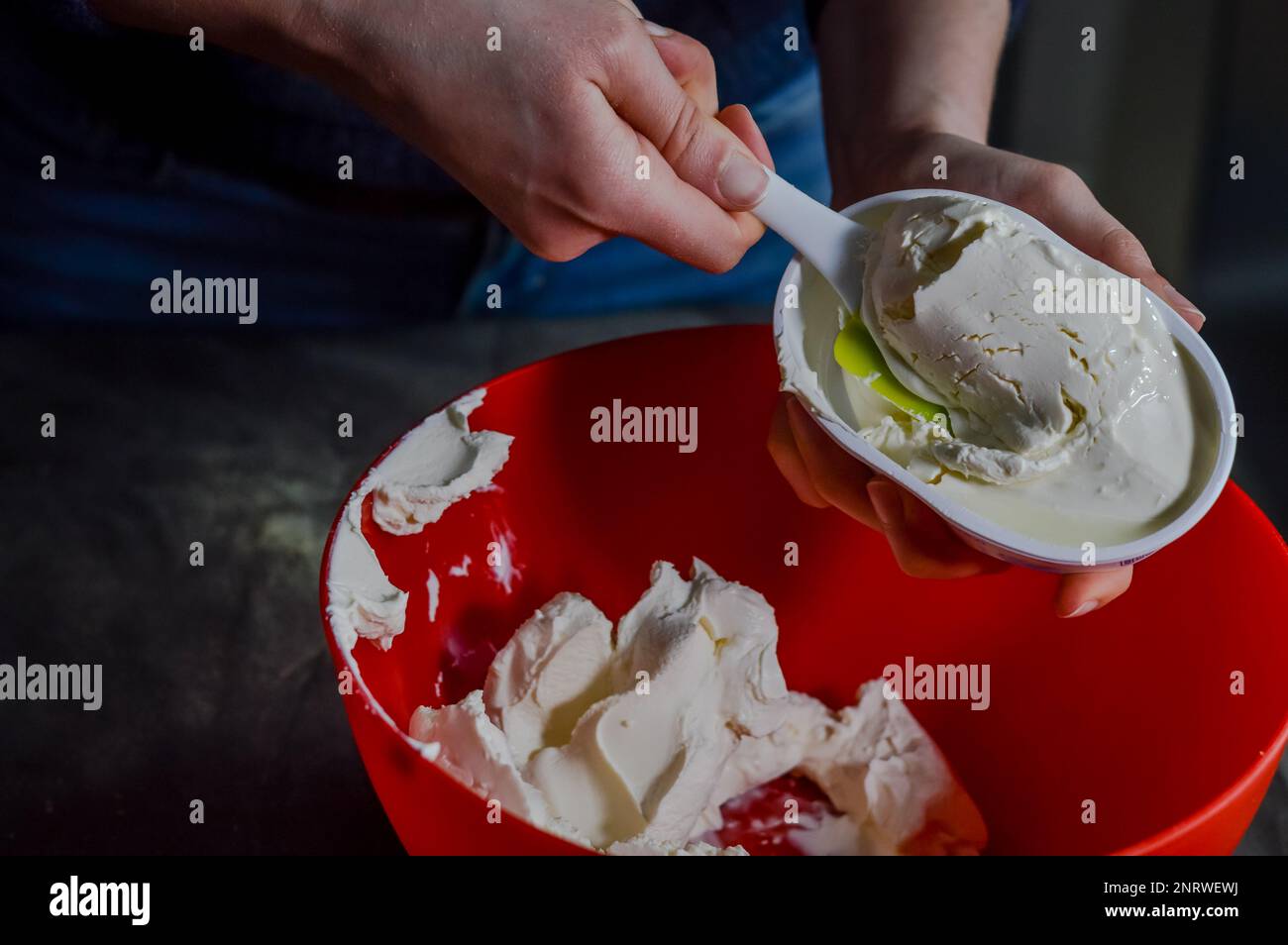 Die Hände entleeren den frischen Weißkäse aus der Verpackung, um ihn zu mischen und einen Käsekuchen zuzubereiten Stockfoto