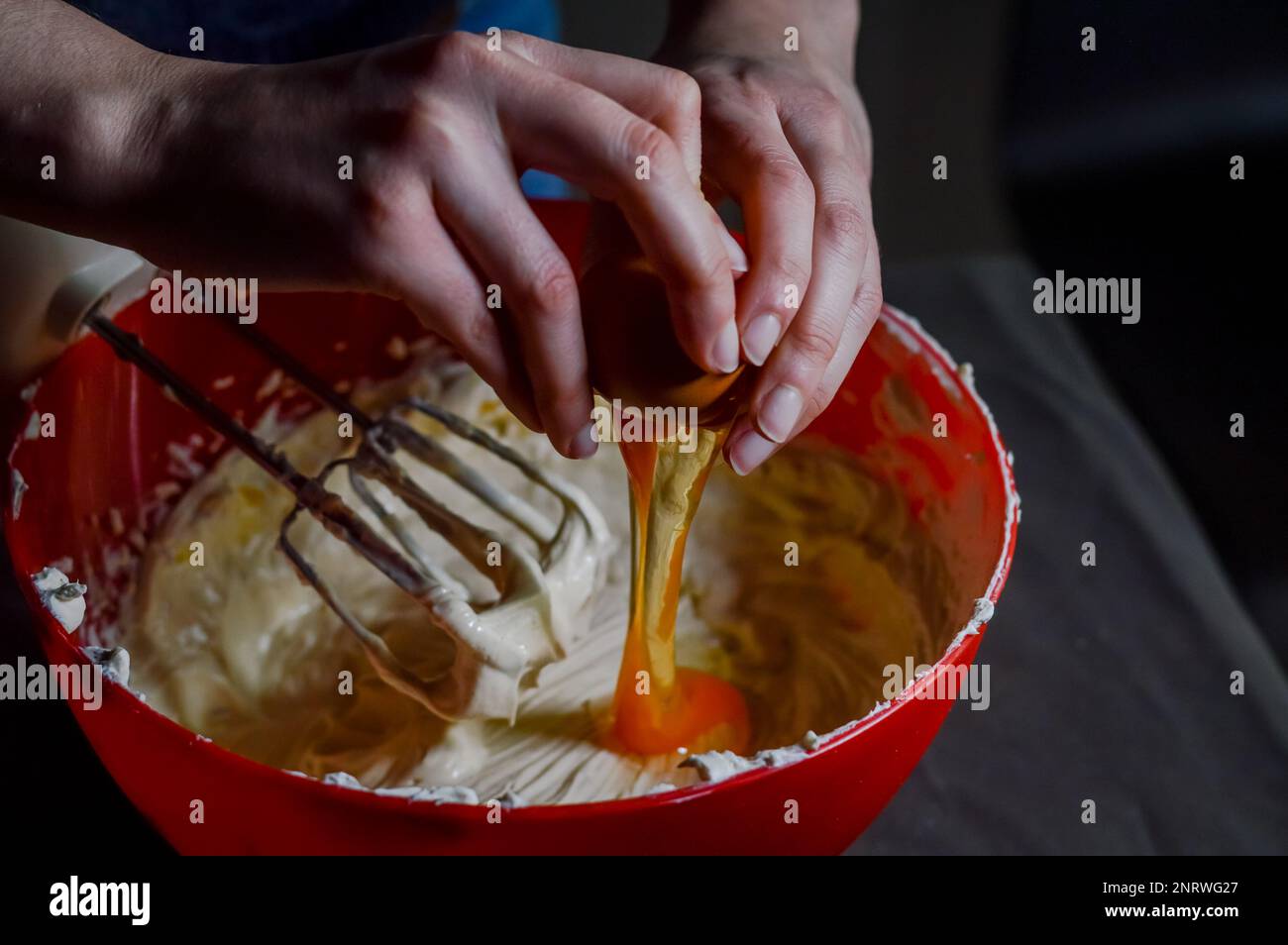 Die Hände geben Ei zu frischem Weißkäse, der zu Käsekuchen-Creme zusammengeschlagen wird Stockfoto