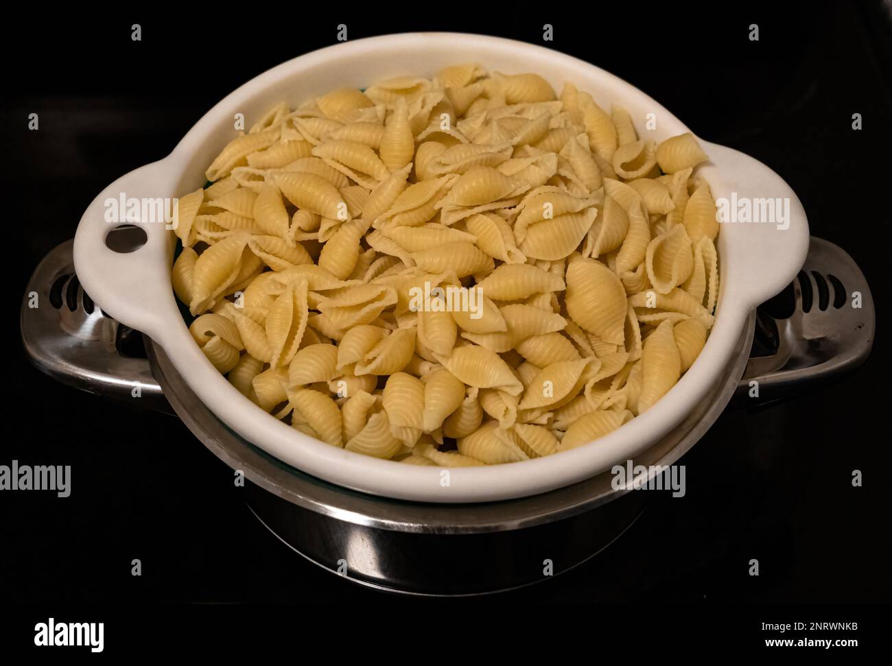 Frisch gekochte Nudelschalen in einem Sieb, das in einen Topf abtropft Stockfoto