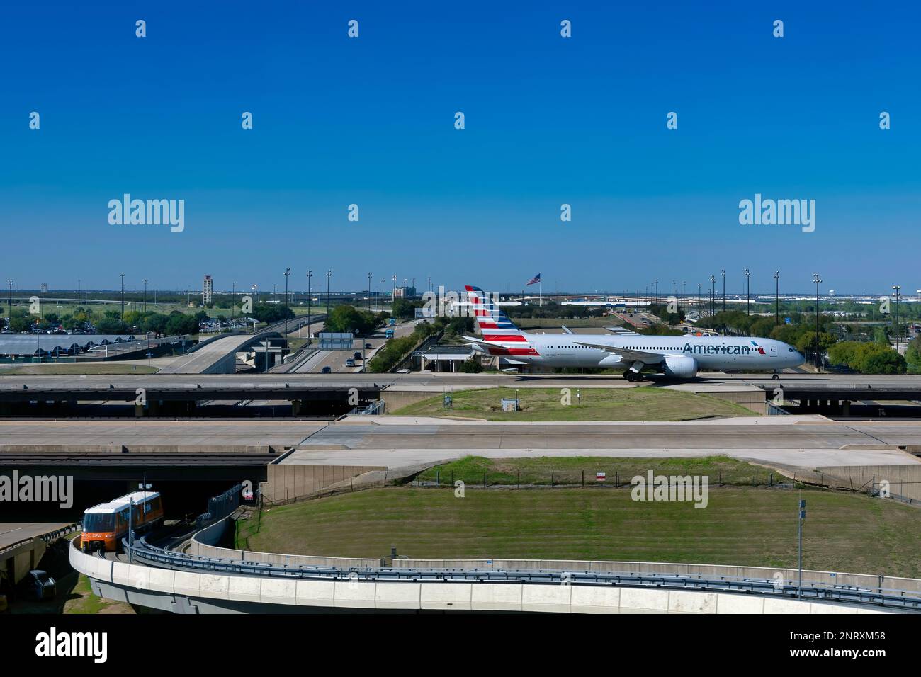 Am Dallas/Fort Worth International Airport in Dallas, Texas, passiert ein Flugzeug eine Brücke, während eine Straßenbahn aus Under kommt. Stockfoto