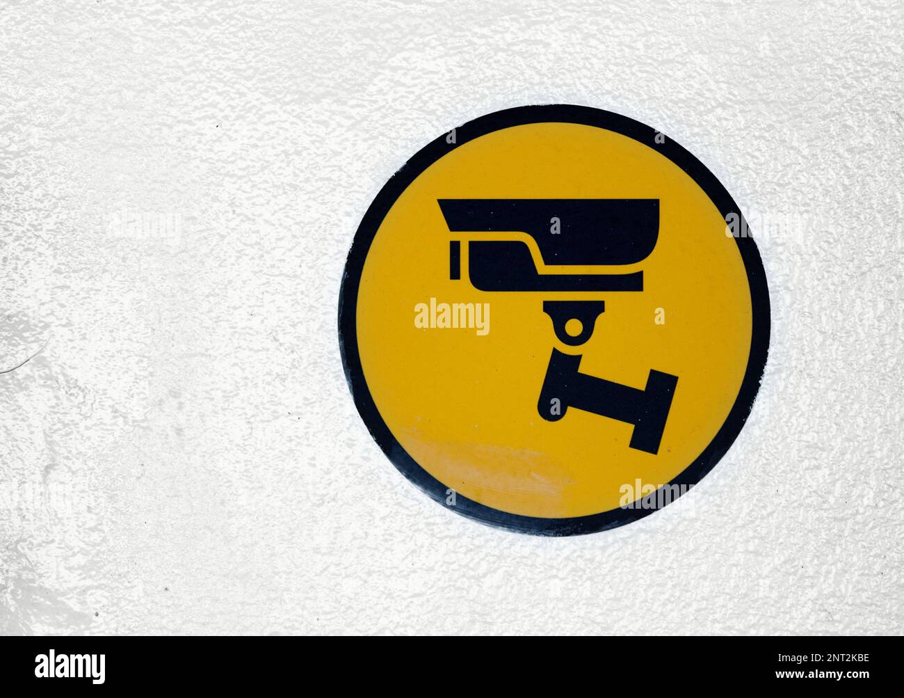 Nahaufnahme eines runden schwarzen und gelben CCTV-Schilds an einer weißen Wand. Stockfoto