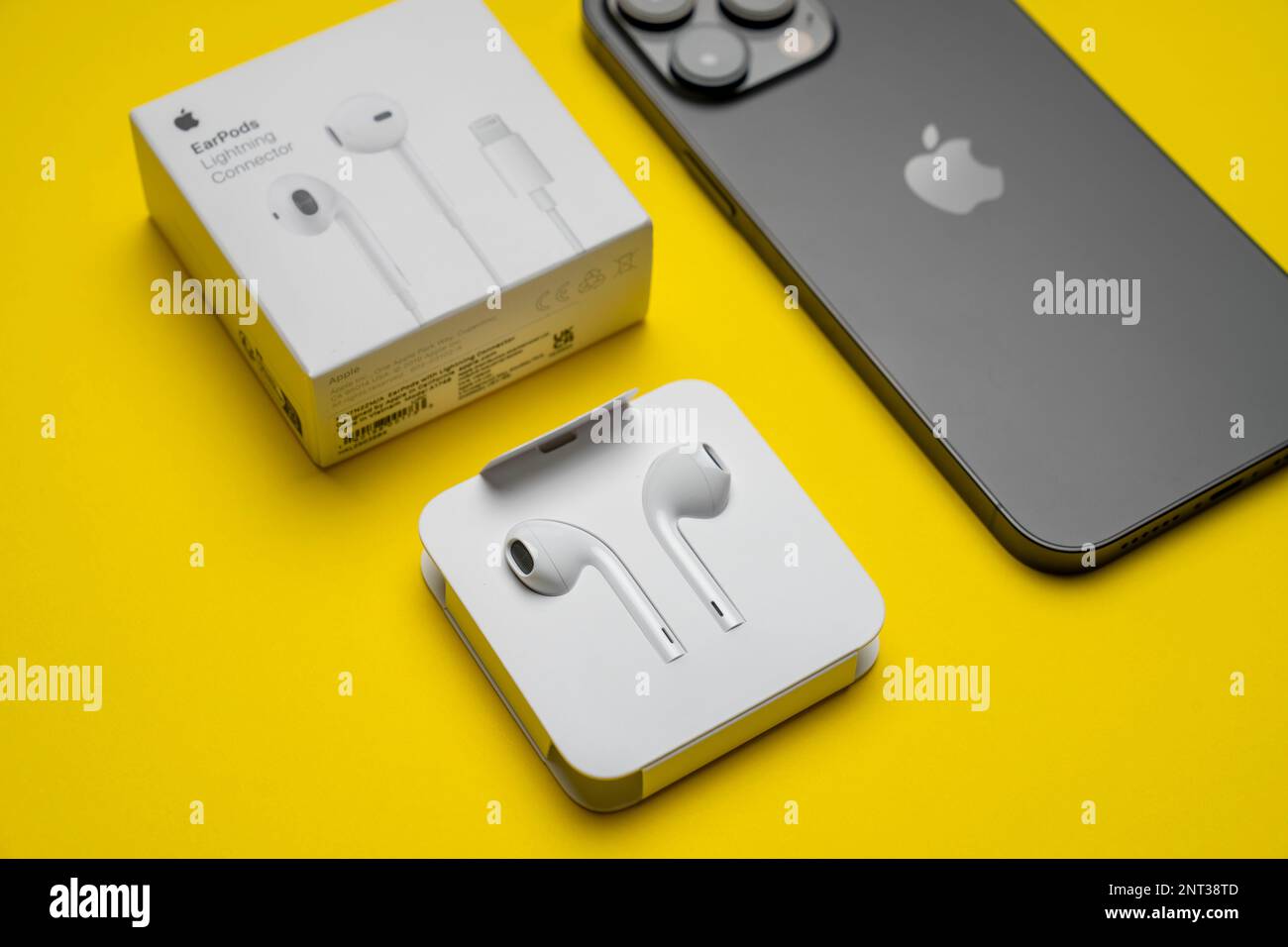 Neues iPhone 14 pro max und Apple Ohrhörer, AirPods weiße Ohrhörer zum Anhören von Musik und Podcasts in einer offenen Verpackung. Isolierter gelber Hintergrund. Budap Stockfoto