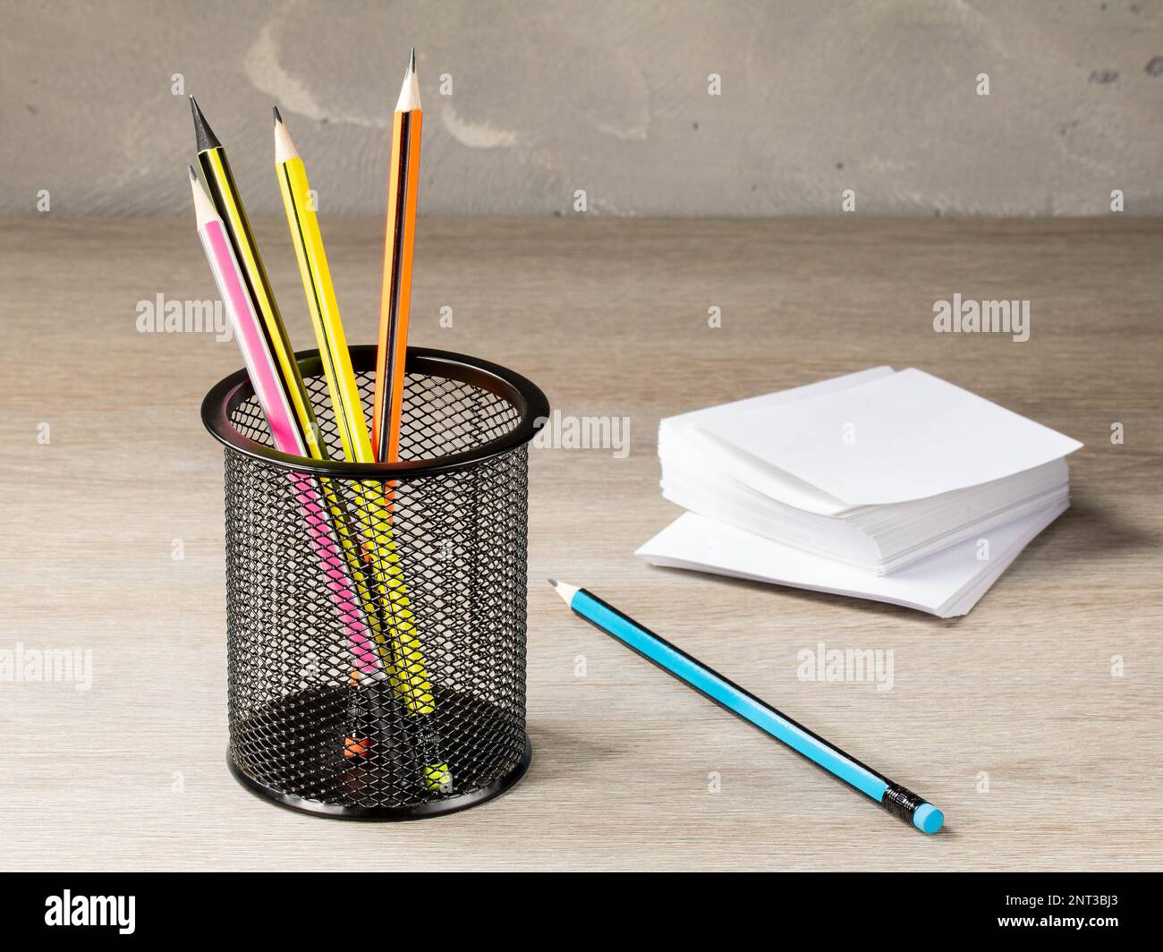 Büromaschinenbehälter aus Netzgewebe mit Bleistiften und einem Stapel Papier für Notizen auf dem Hintergrund des Bürotischs. Stockfoto