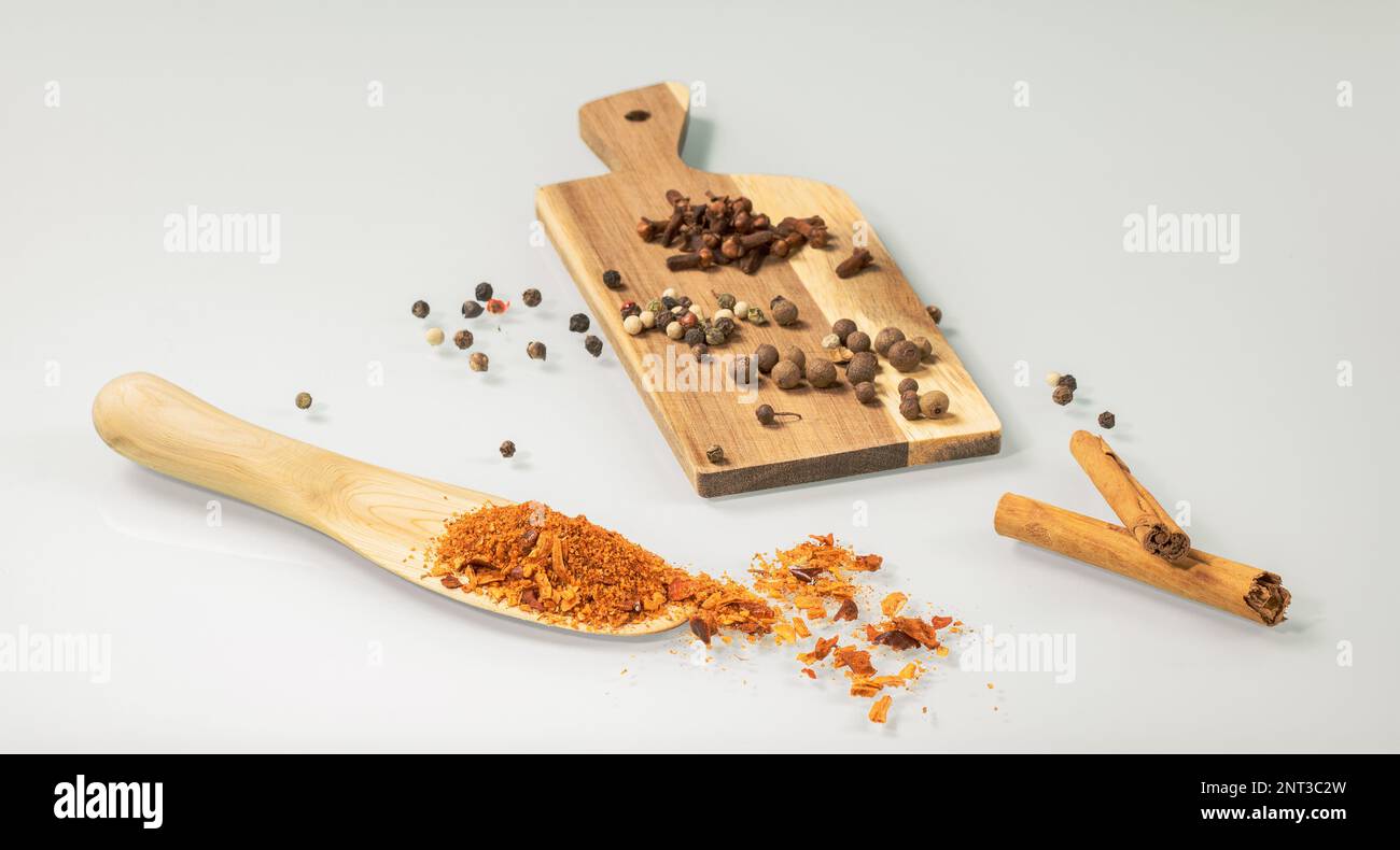 Küchen-Stillleben. Holzlöffel und Mini-Brett mit verschiedenen Gewürzen - Pfeffer, Nelken, indische Gewürze, Zimt auf hellem Spiegelhintergrund Stockfoto