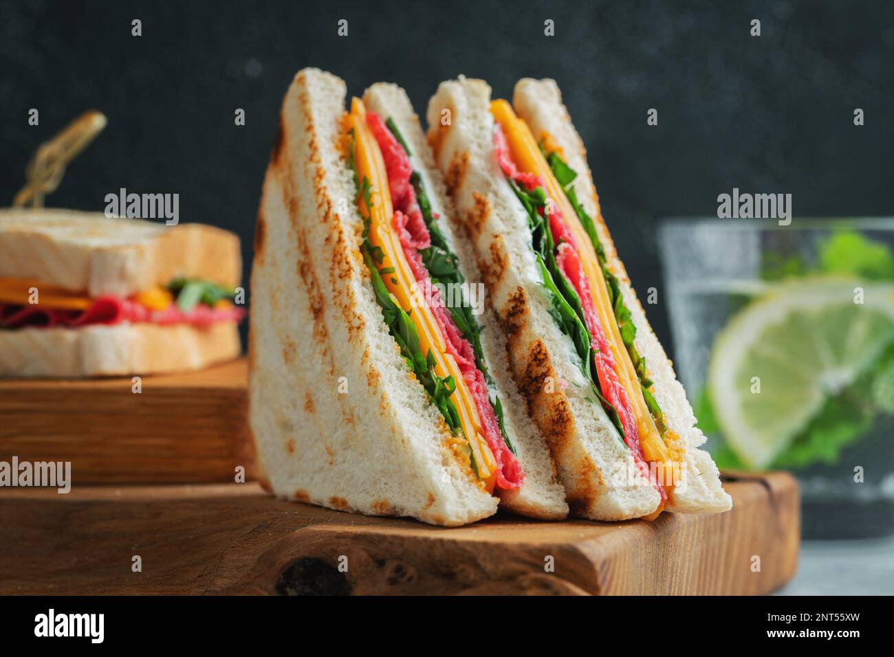 Zwei hausgemachte Sandwiches mit Wurst, Käse und Rucola auf hellem Betonhintergrund. Das Konzept eines schnellen Essens oder Snacks bei der Arbeit oder in der Schule. Stockfoto