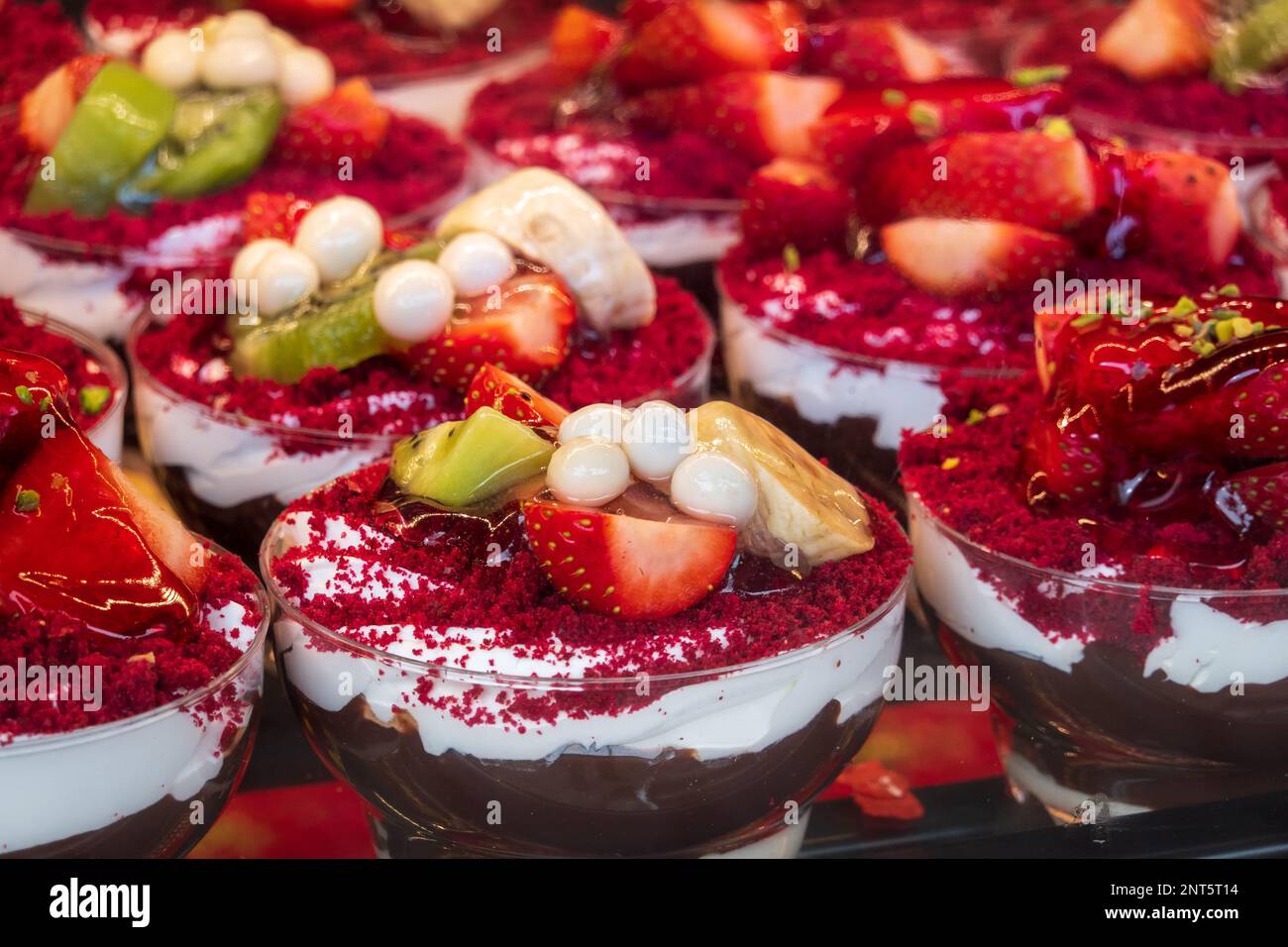 Ein großer Haufen köstlicher Desserts mit Schokoladencreme und Joghurt, dekoriert mit Scheiben von frischer Erdbeer-Banane und Kiwi in Patisserie Stockfoto