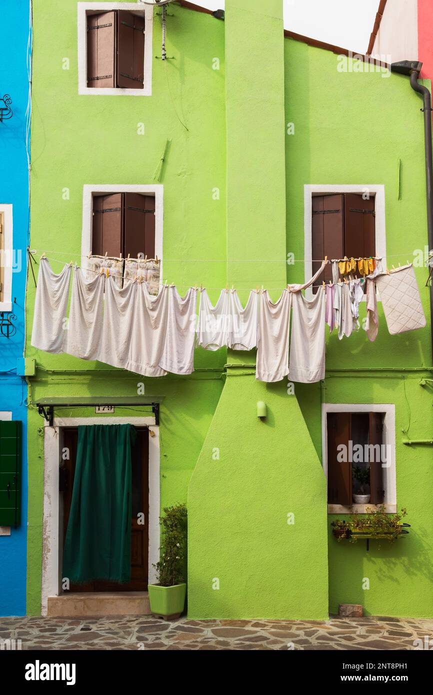 Grüne Stuckhausfassade mit Vorhang über der Eingangstür und gewaschener Kleidung an der Wäscheleine, Burano Island, Lagune Venezian, Venedig, Italien. Stockfoto