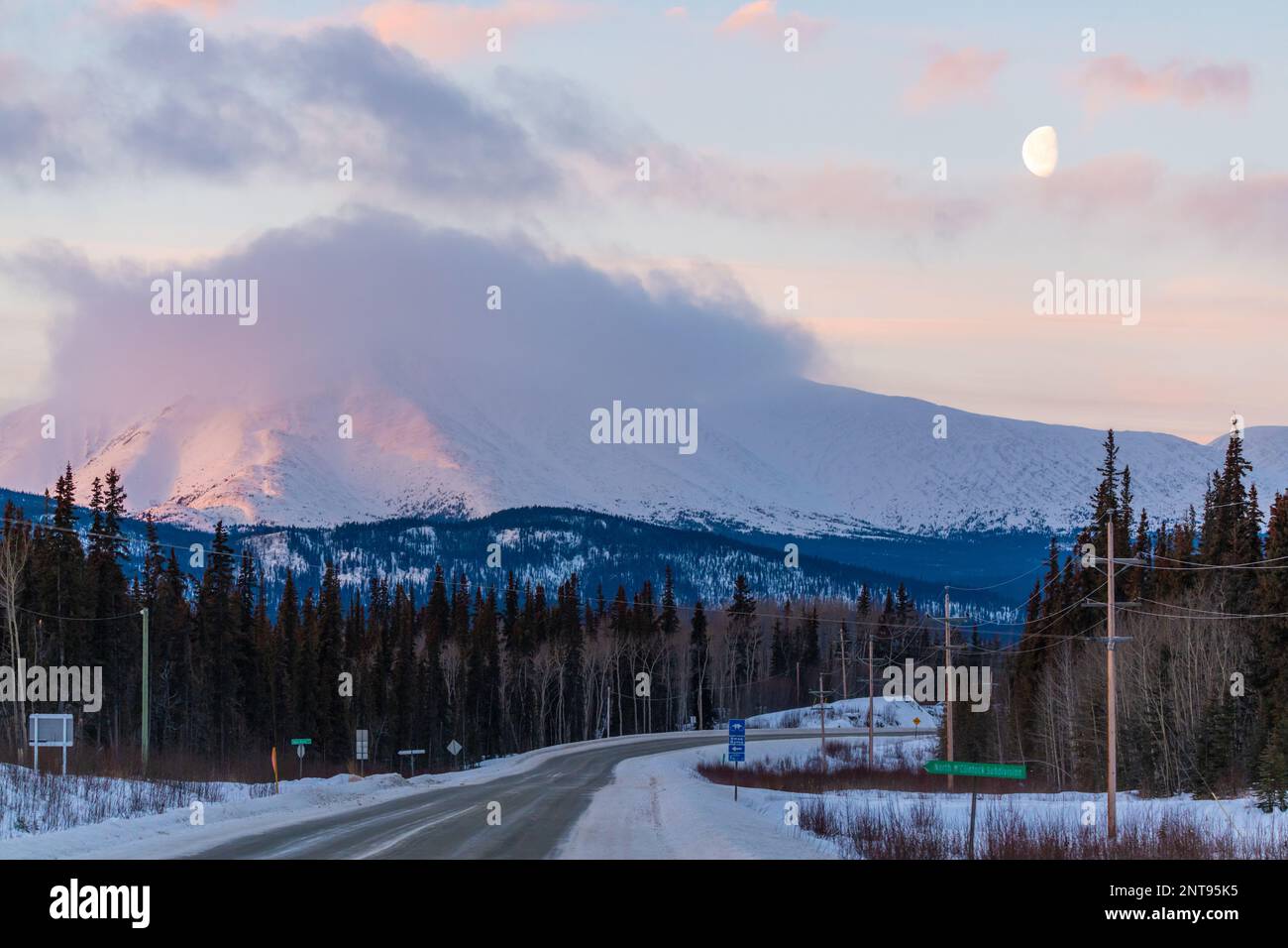 Pastellrosa Sonnenaufgang entlang des Alaska Highway in der Wintersaison mit Monduntergang über der Wildnis. Stockfoto