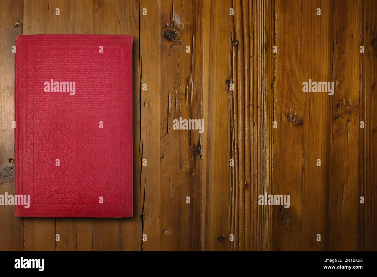 Nahaufnahme eines roten Buches auf einem braunen Holzschreibtisch. Stockfoto