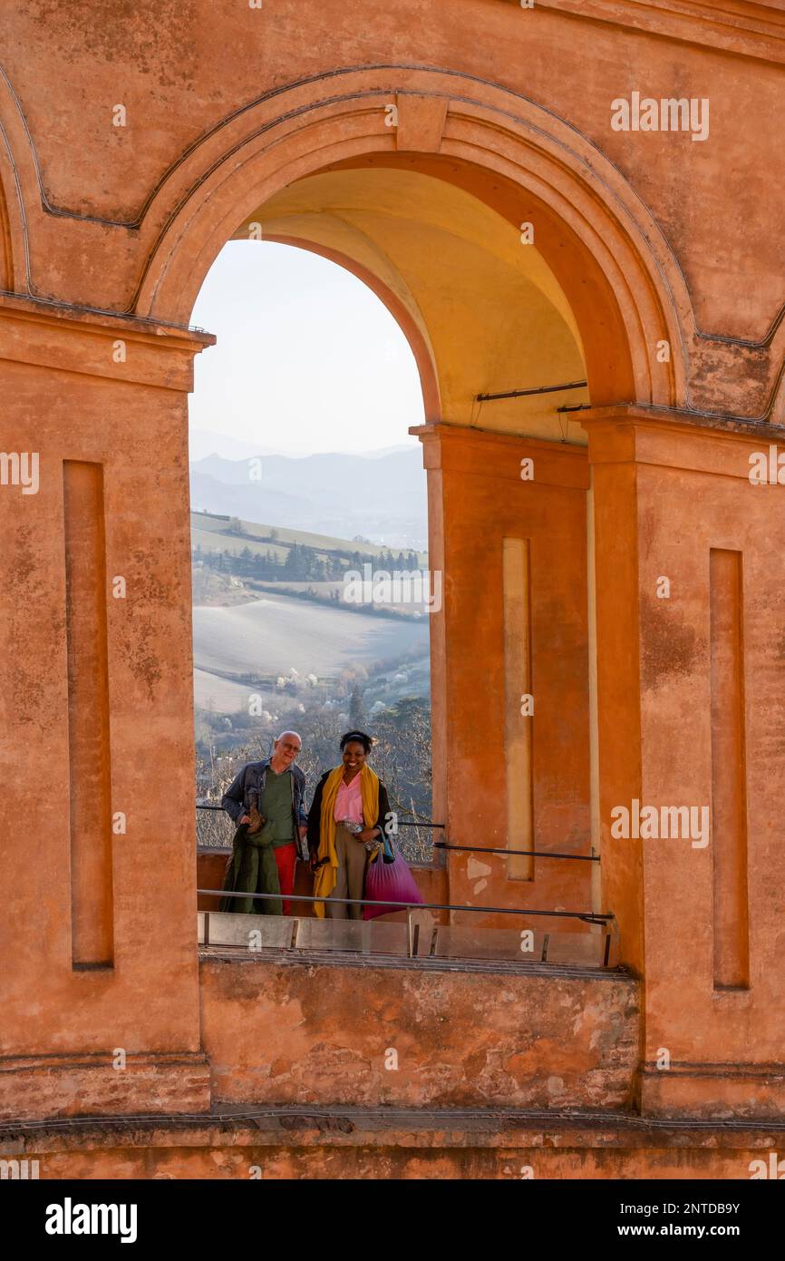 Ein Paar lächelt vor der Kamera durch den Torbogen in Portico di San Luca, Santuario della Madonna di San Luca, Bologna, Emilia-Romagna, Italien Stockfoto