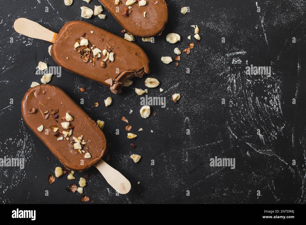 Milchschokolade Eis am Stiel mit Haselnüssen. Nahaufnahme. Eis am Stiel bedeckt mit Schokolade, Stöcken und schwarzem Steinmarmorhintergrund. Platz für Text. Stockfoto