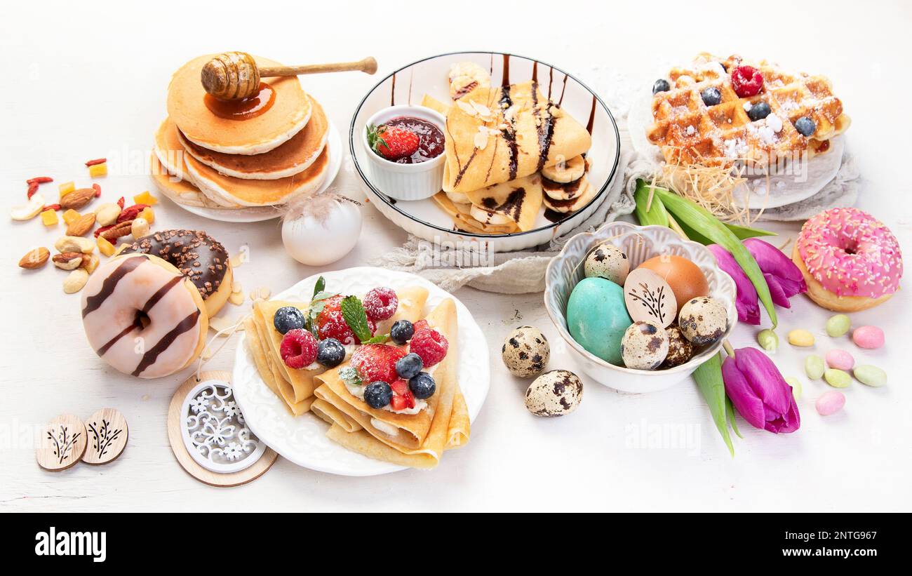 Süßer Ostertisch. Pfannkuchen, Crepes, Waffeln und Donuts mit frischen Beeren, Nüssen und Belag. Ostern traditionelle, natürliche bunte Eier. Stockfoto