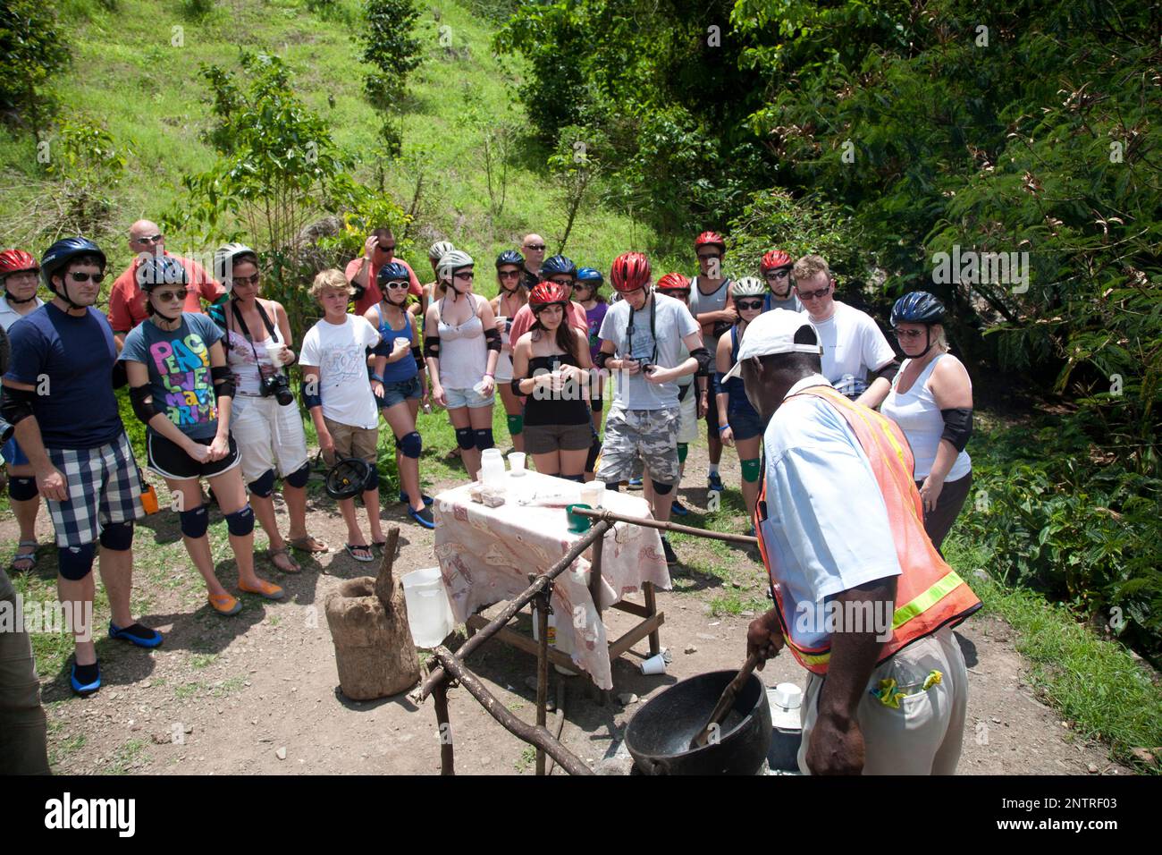 Mountainbiker halten an, um die traditionelle Röstmethode von Kaffeebohnen als touristische Aktivität zu beobachten, Dry Harbour Mountains, Jamaika. Stockfoto