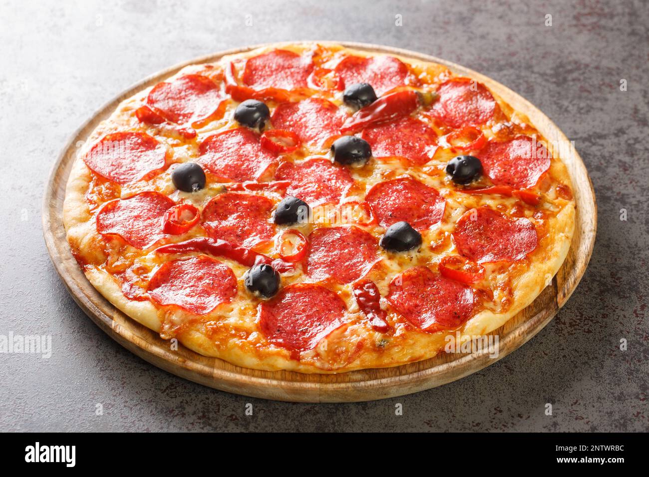 Köstliche klassische Pizza Devil mit Peperoni-Wurst, Käse, Tomatensoße, Chili-Paprika und schwarzen Oliven aus nächster Nähe auf einem Holzbrett auf dem Tisch. Ge Stockfoto