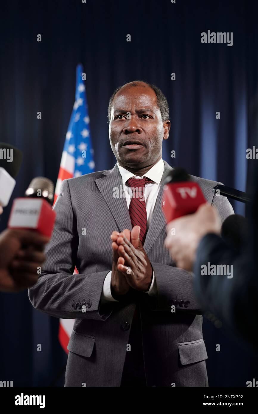 Reifer afroamerikanischer Stellvertreter in formeller Kleidung, der die Hände zusammenhält, während er Journalisten auf der Pressekonferenz interviewt Stockfoto