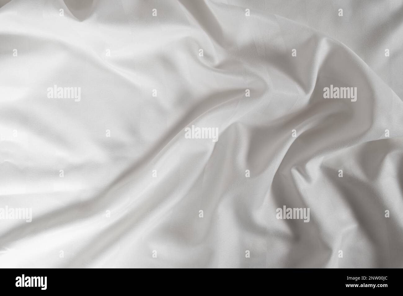Satiniertes, weißes, zerknittertes Material, Draufsicht. Natürliche Bettwäsche, Laken, abstrakter Hintergrund aus luxuriösem Stoff, wellenförmige Falten Stockfoto