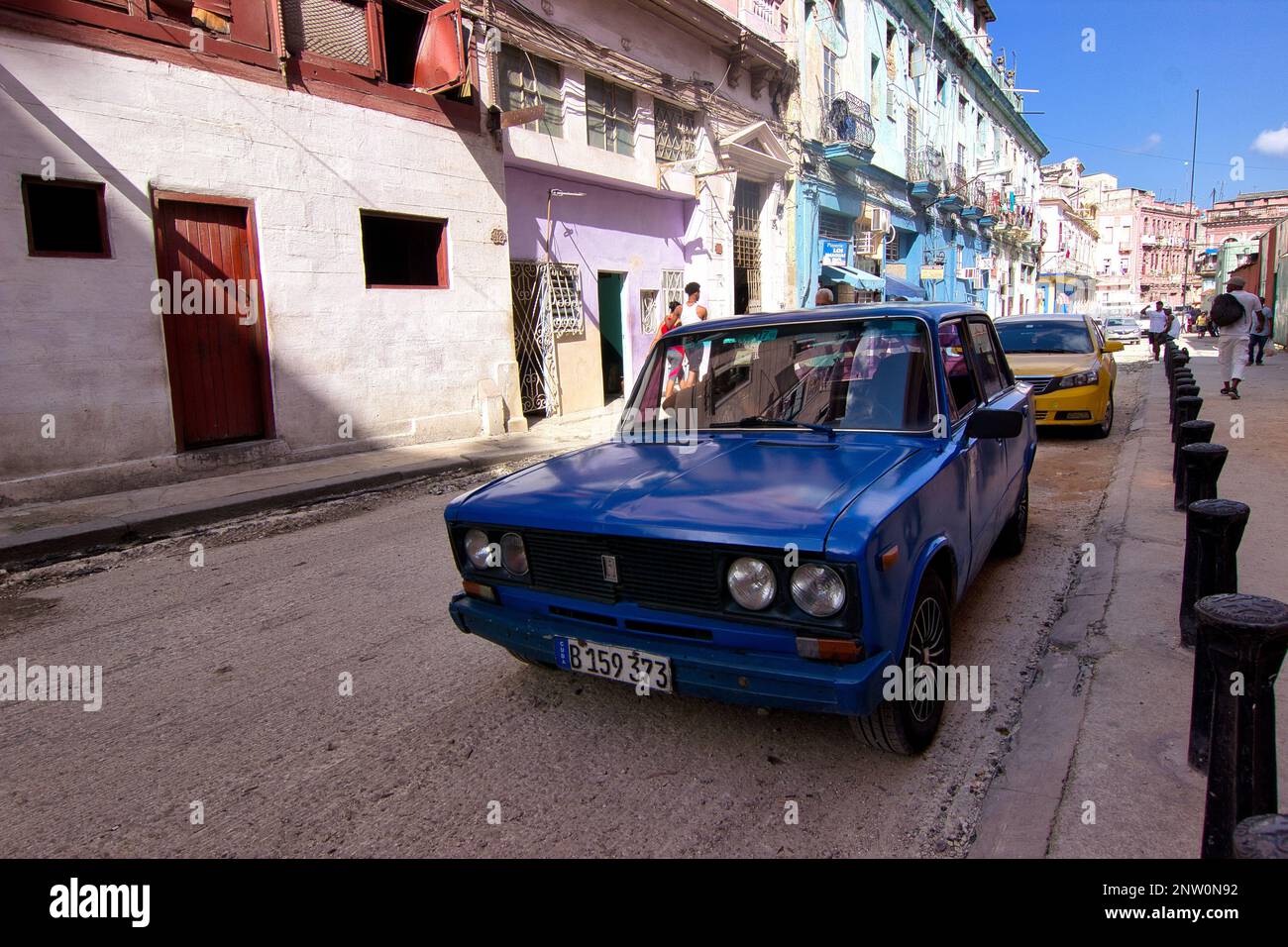 Ein blauer Oldtimer in einer Gasse mit alten, bunten Gebäuden in Havanna, Kuba. Stockfoto