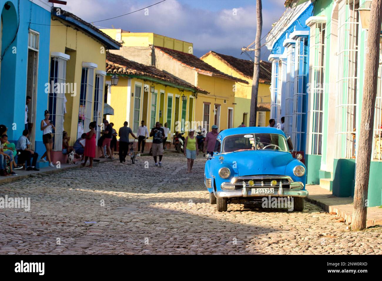 Ein blauer Oldtimer in einer Gasse mit alten, bunten Gebäuden in Trinidad, Kuba, Menschen im Hintergrund. Stockfoto