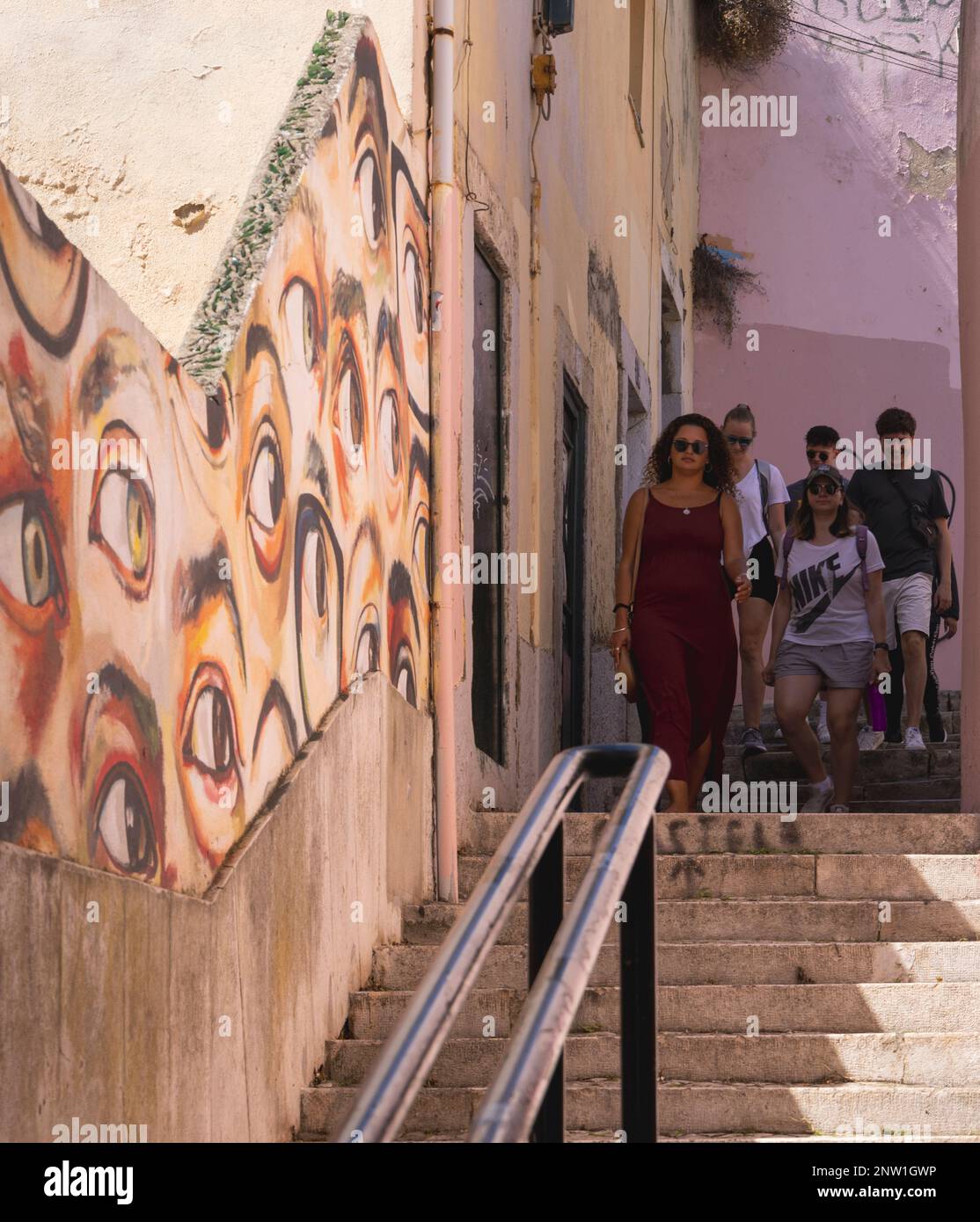 Lissabon, Portugal. Leute steigen Treppen in einer engen Gasse hinab. Die Wand ist mit Graffiti von beobachtenden Augen bemalt. Stockfoto