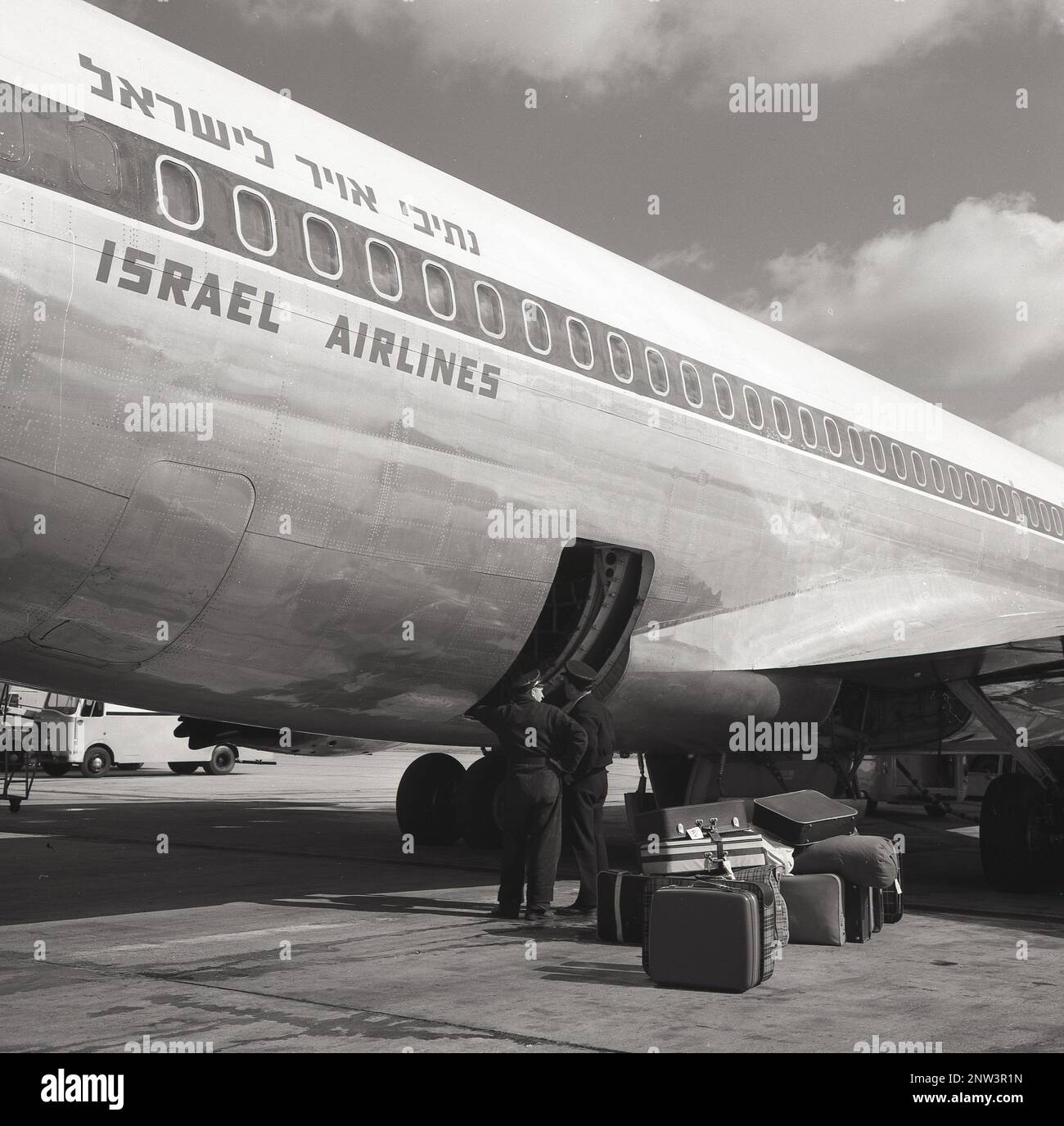 1960er Jahre, historisch, Passagiergepäck am Boden, als uniformierte Gepäckcrew an einem offenen Eingang eines Israel Airlines Boeing Jet-Flugzeugs am London Airport, England, Großbritannien steht. Stockfoto