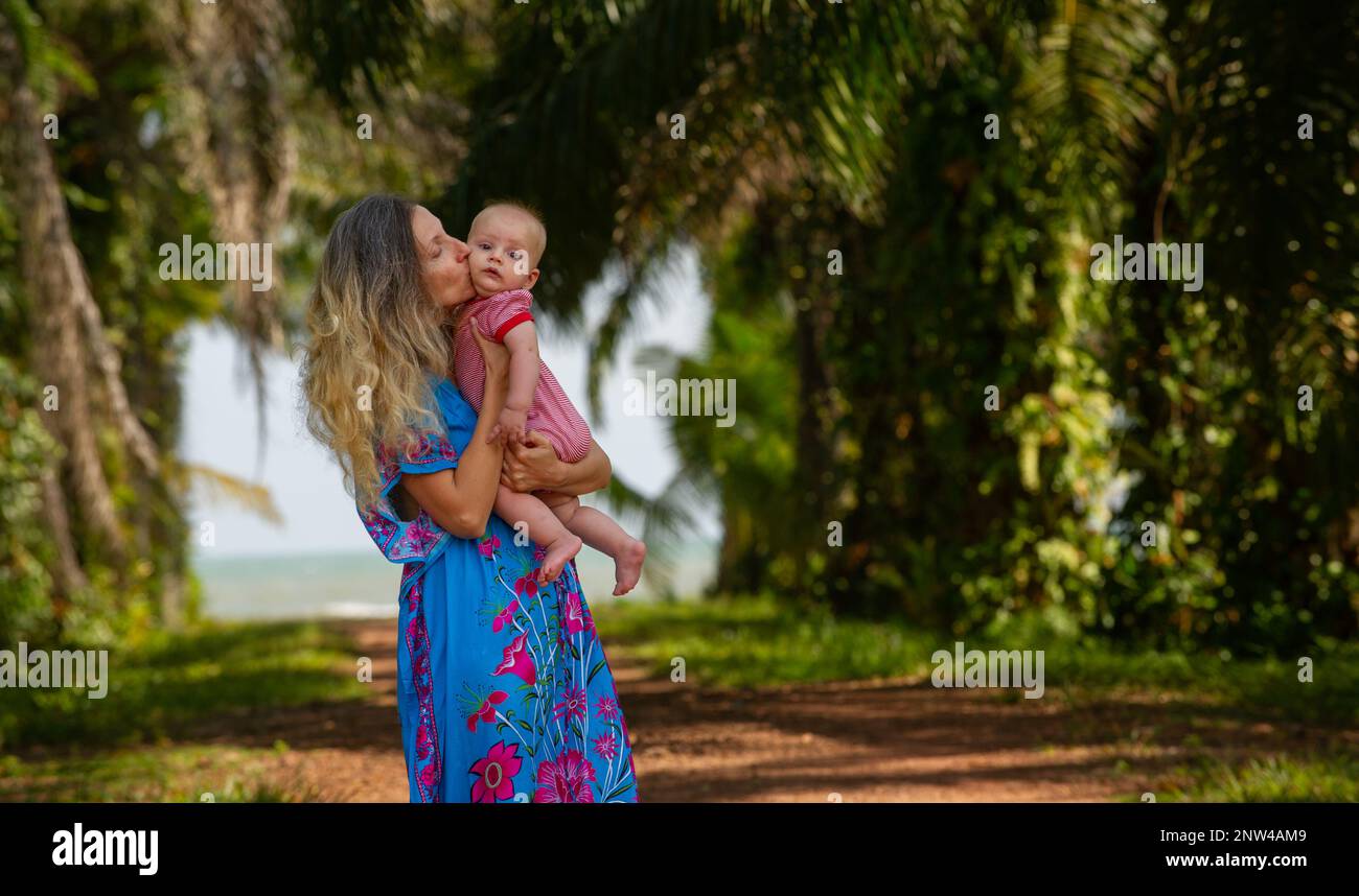 Mutter mit niedlichem Baby im Urlaub in Thailand und spaziert durch blau gekleidete Palmen Stockfoto