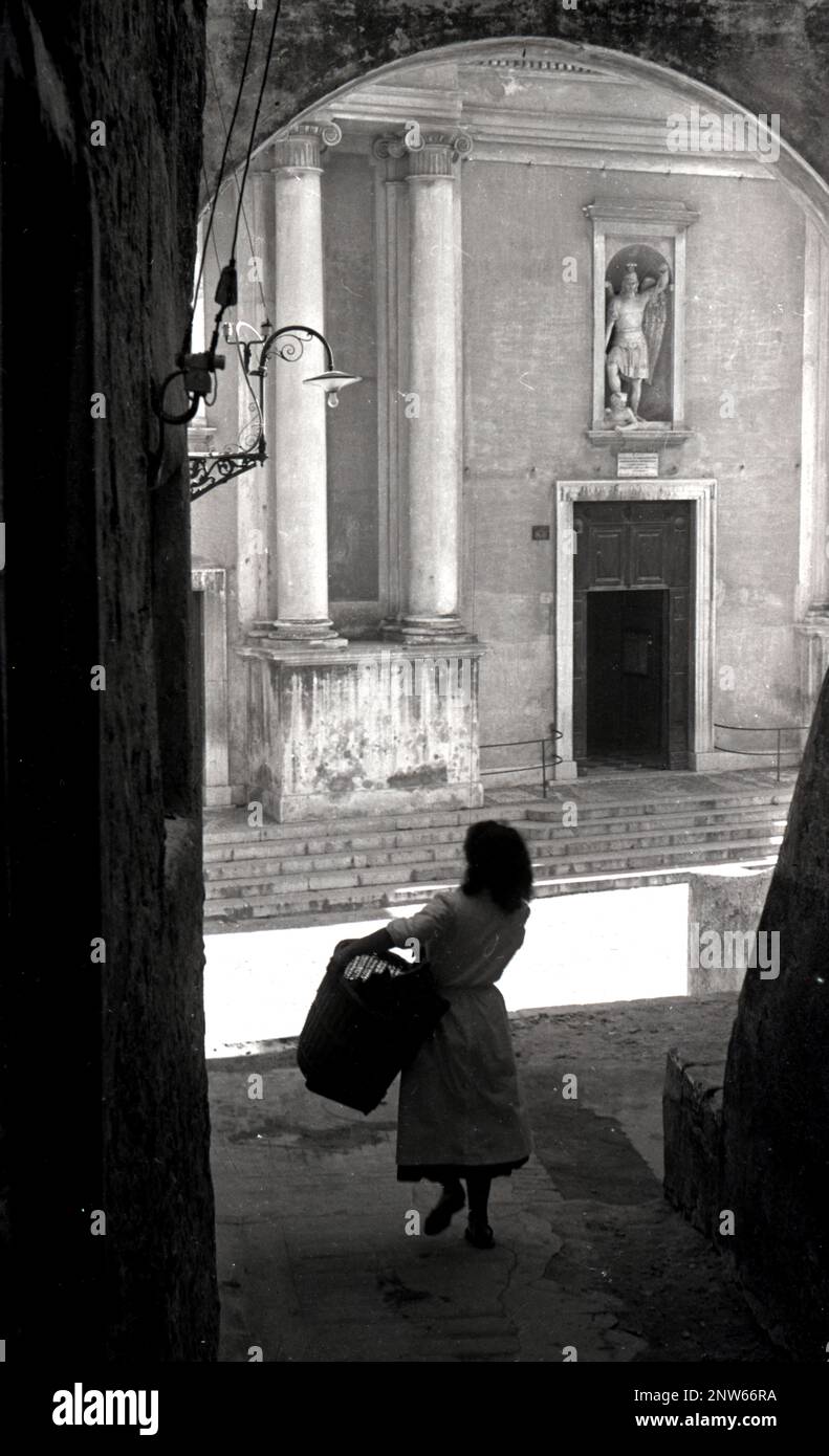 Eine junge italienische Frau trägt einen Korb durch die verlassenen Straßen von Rom, Italien, in den 1930er Jahren, vielleicht auf dem Weg zum Markt. Stockfoto