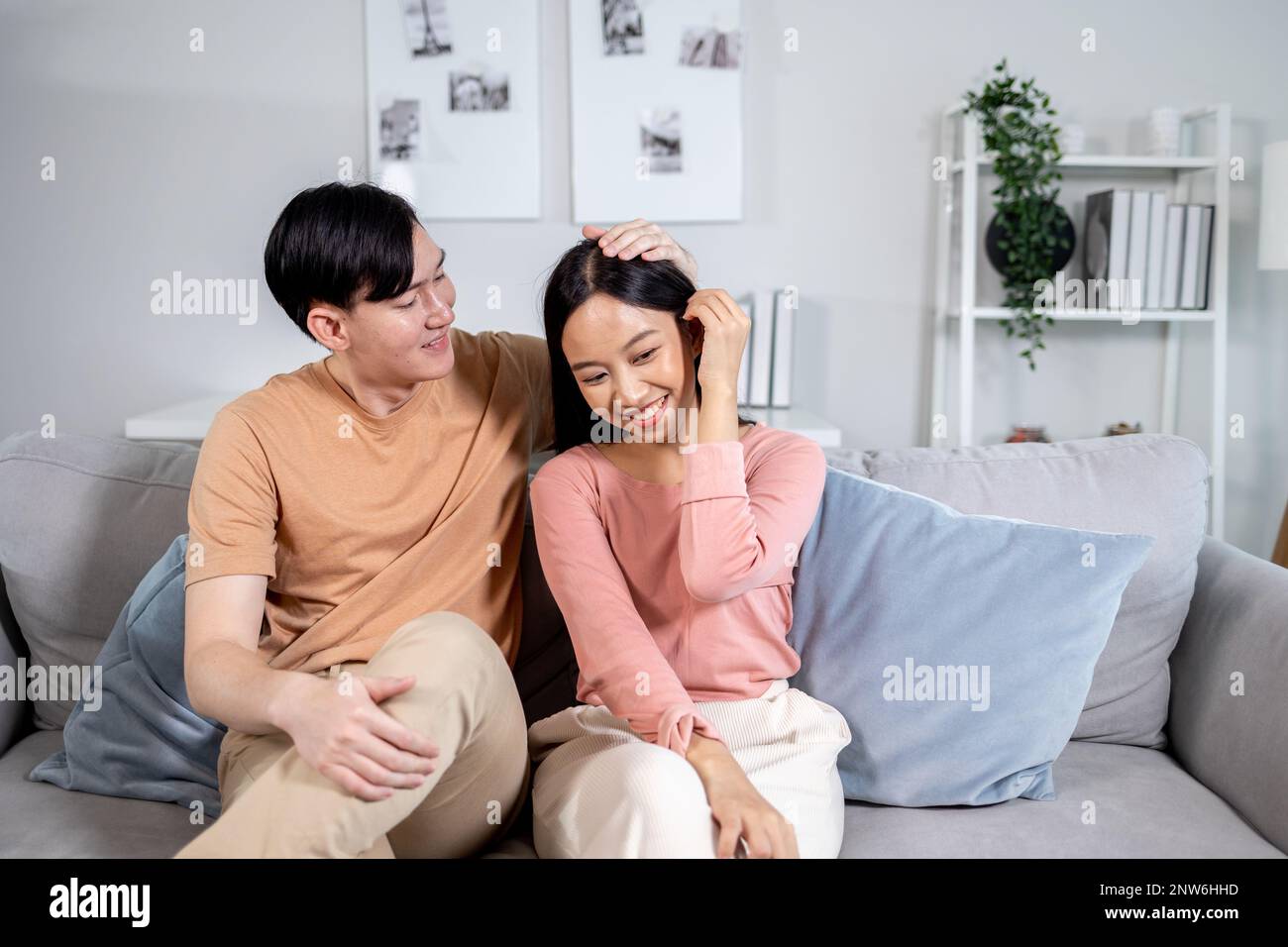 Ein junges asiatisches, glückliches Paar, das lächelt und auf der Couch im Wohnzimmer zu Hause sitzt. Freund und Freundin umarmen und entspannen Stockfoto