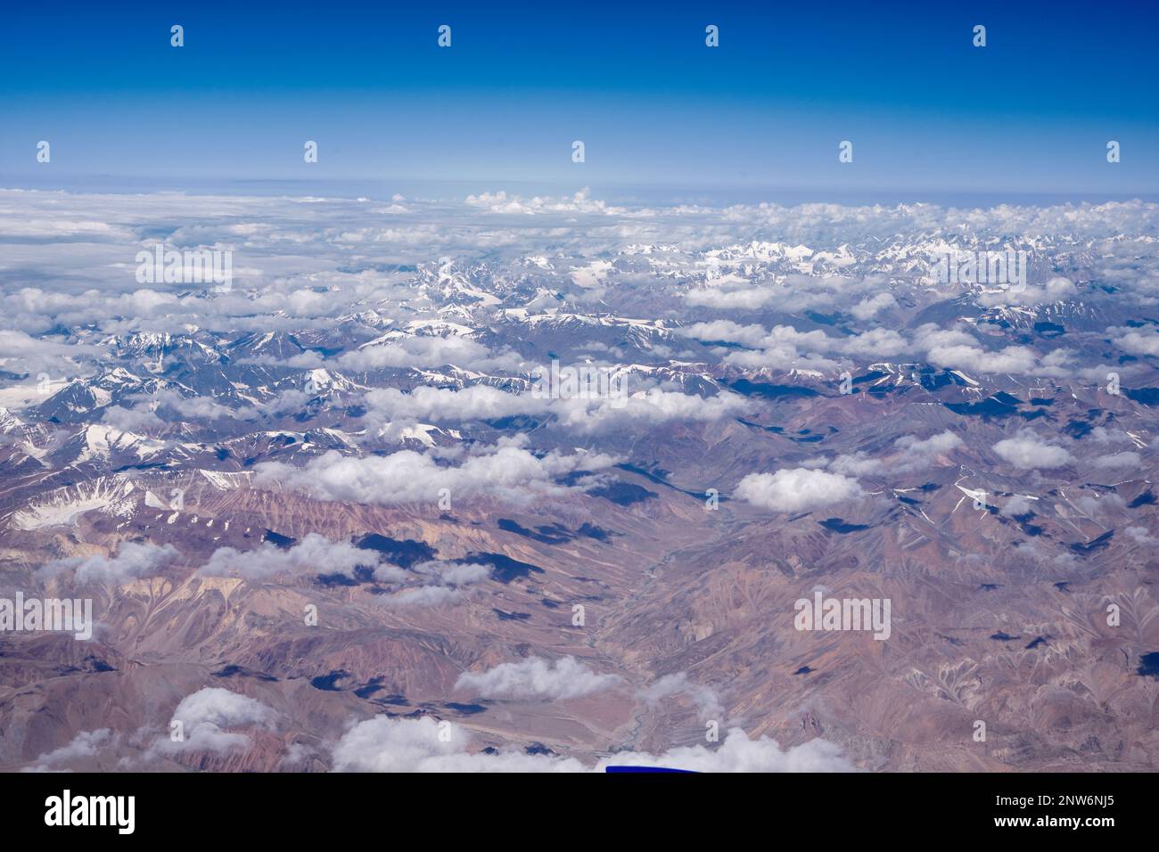 Blick von oben auf die braunen Berge mit Wolken und Horizontlinie aus dem Inneren des Flugzeugs Stockfoto