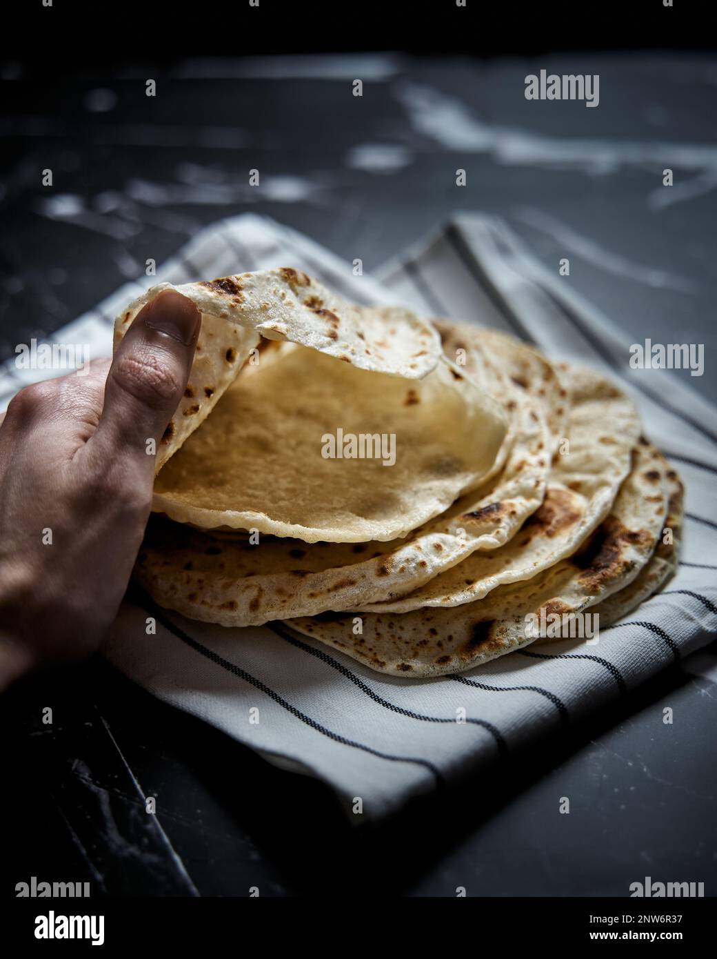 Gebratenes Pita-Brot in der Pfanne auf dunklem Hintergrund. Pita-Brot mit der Hand öffnen und Lufteinschlüsse zeigen Stockfoto